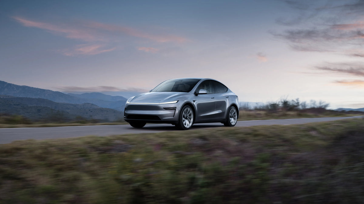A silver electric sedan driving along a road against a backdrop of mountains at dusk.