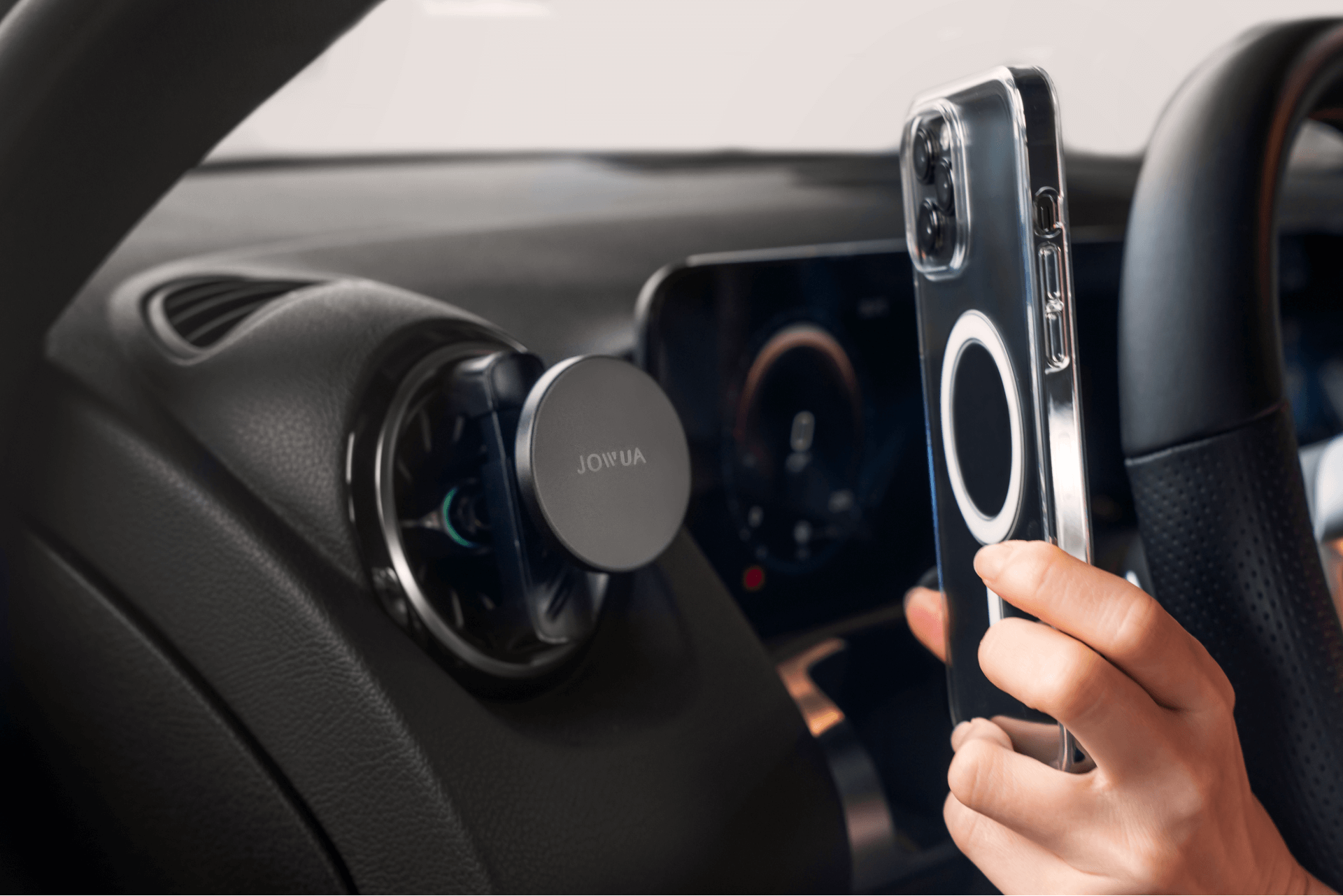 A hand holding a clear phone case near a magnetic phone holder mounted on a car's air vent. The dashboard and part of the steering wheel are visible.
