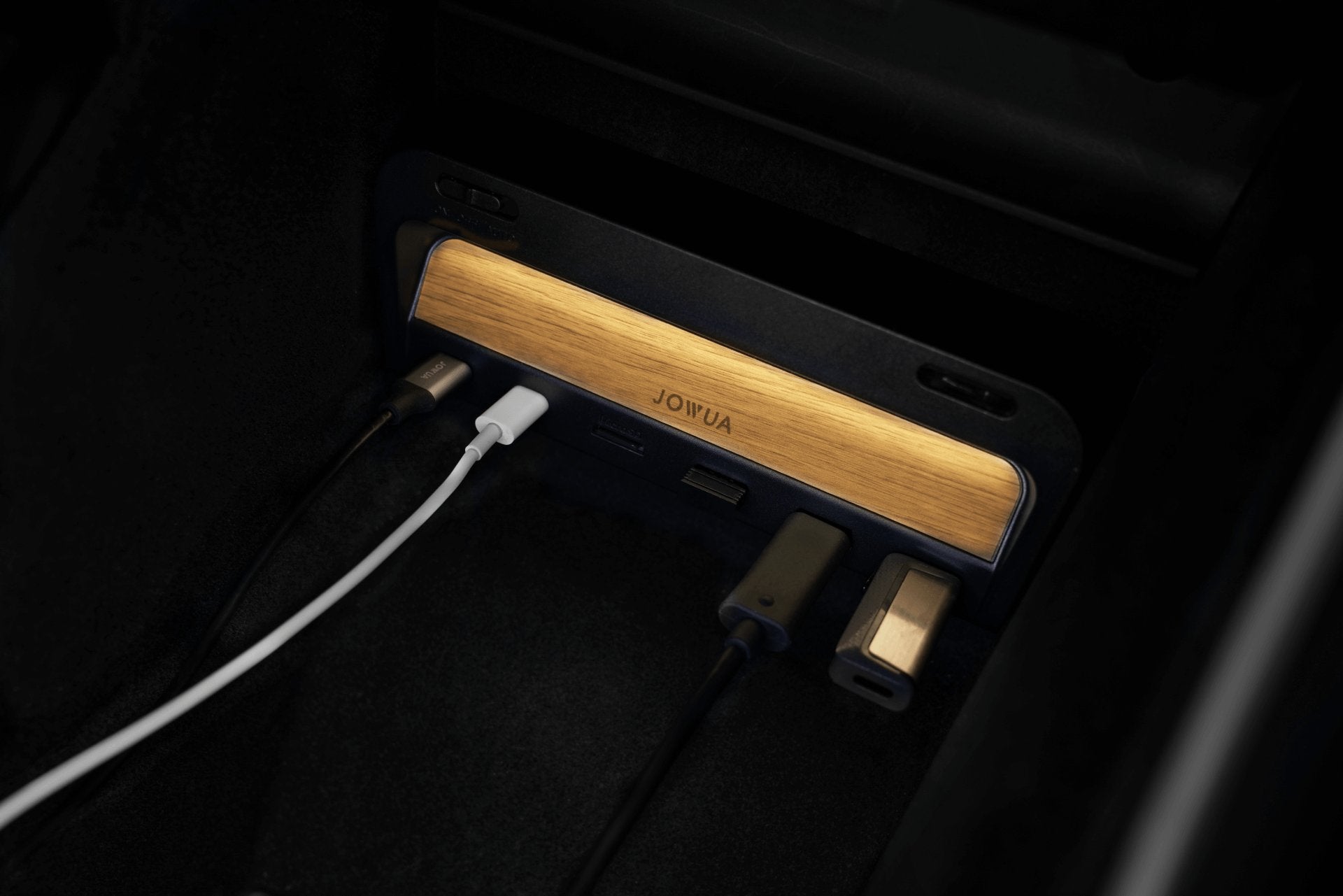A variety of cables and USB devices plugged into a stylish black and wood-accented charging hub with multiple ports, located in a car's center console.