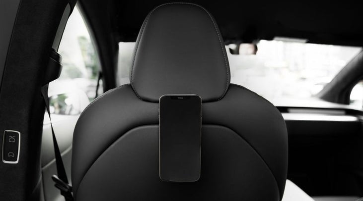 A smartphone is mounted on the back of a Tesla Model Y's black leather headrest, facing the rear seats. The modern, well-lit cabin showcases JOWUA's Premium Interior Essentials Set – Model Y Juniper (2025+).