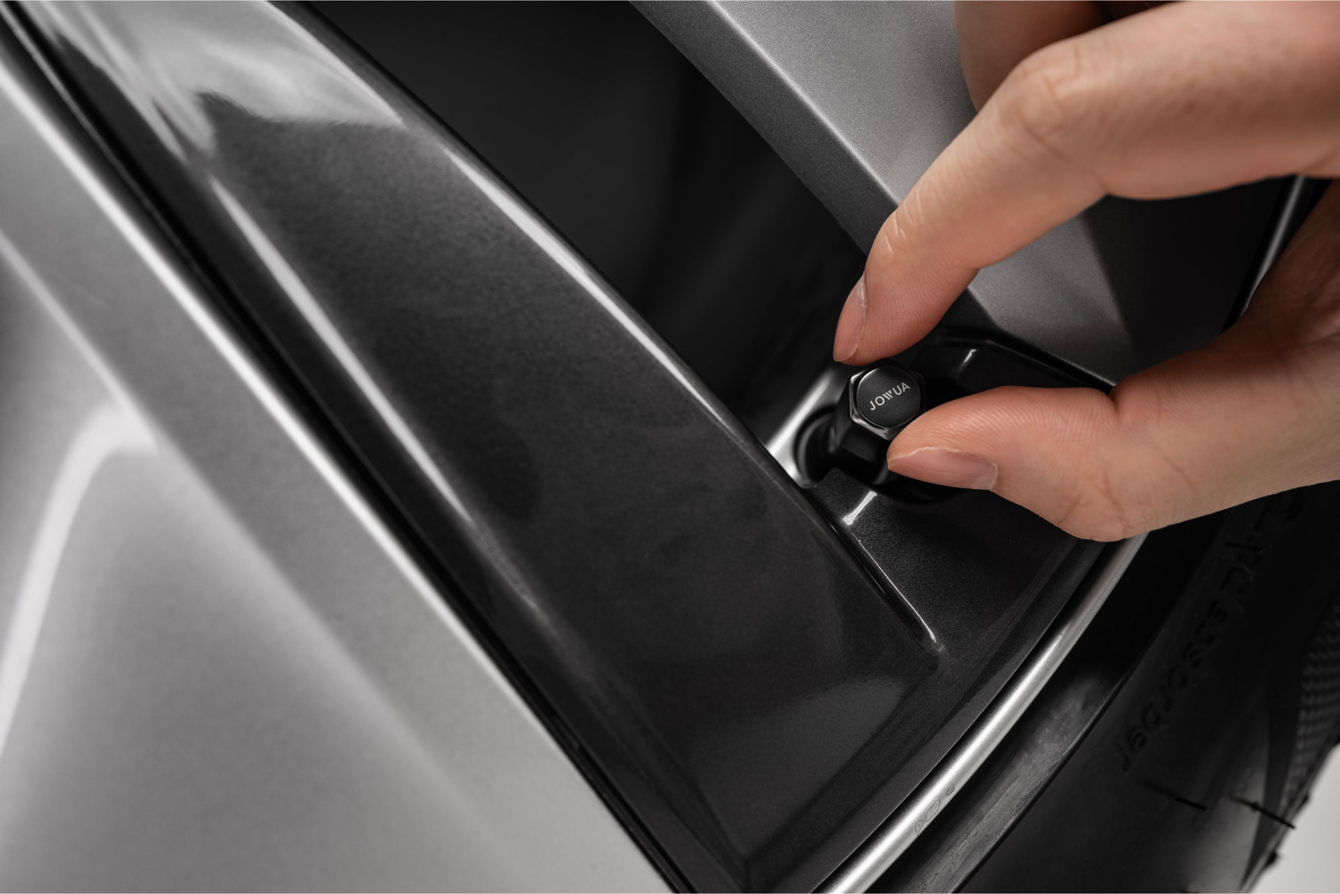 A hand adjusts a knob labeled "close" on a sleek, gray metallic surface reminiscent of the JOWUA Tire Valve Caps. The surrounding area features smooth, reflective finishes and boasts zinc alloy components for enhanced durability and style.