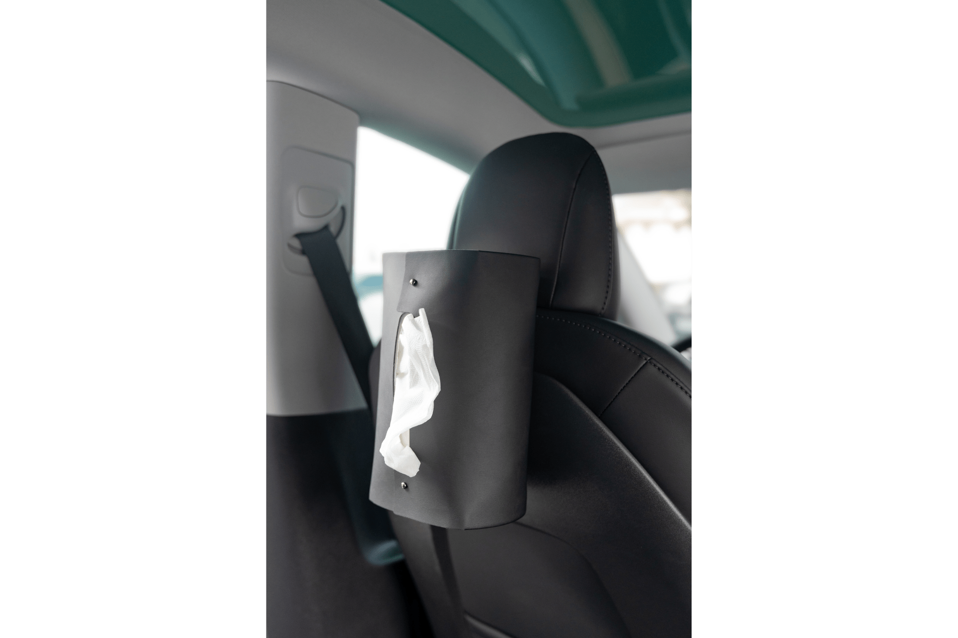 A MagSafe Tissue Box Cover from JOWUA is attached to the back of a Model 3/Y car seat, with a tissue partially pulled out. The interior of the car is visible, showcasing the seat's headrest and a seatbelt.