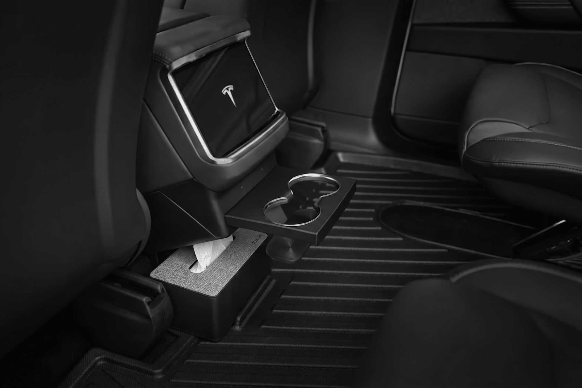 Black and white photo of a Tesla’s back seat showcases JOWUA Model X All-Weather Floor Liners, center console with a tissue box, fold-out cup holder, and sleek seats for a clean, modern interior.