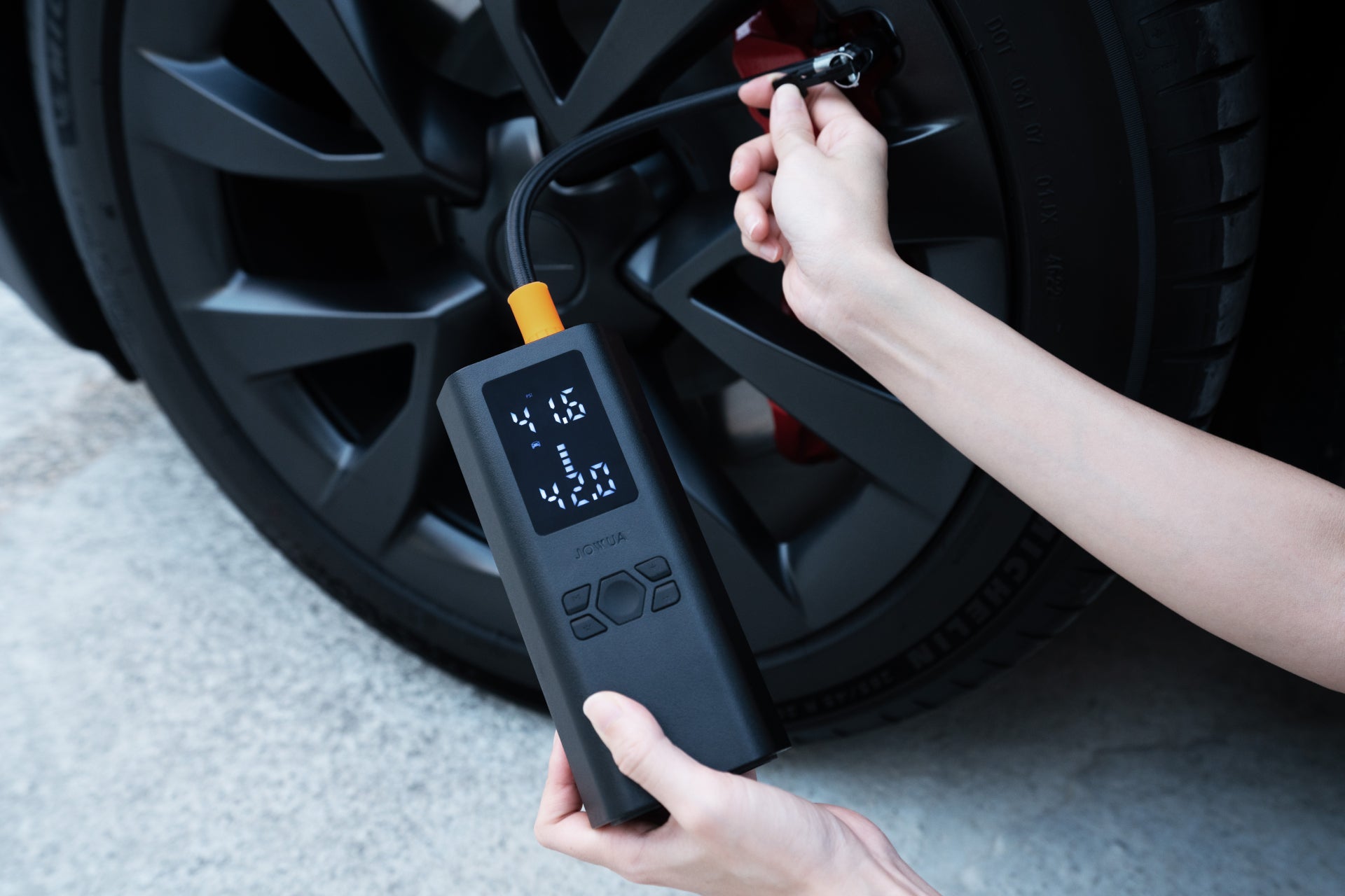 A person uses the JOWUA Portable Air Compressor + Charging Solution Kit to inflate Tesla tires, connecting the hose to the valve while checking pressure on the LED screen.