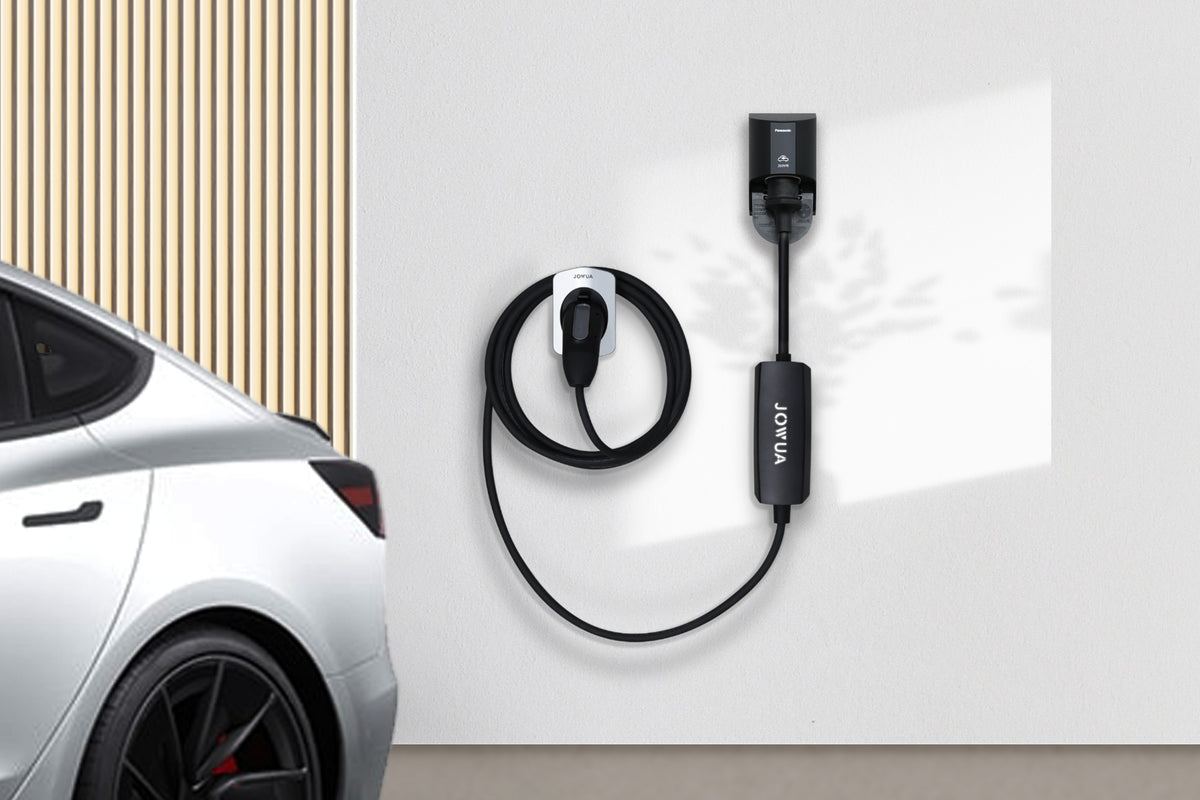 A JOWUA テスラ用 NACS モバイルコネクター charging cable and control unit mounted on a wall next to a parked car.