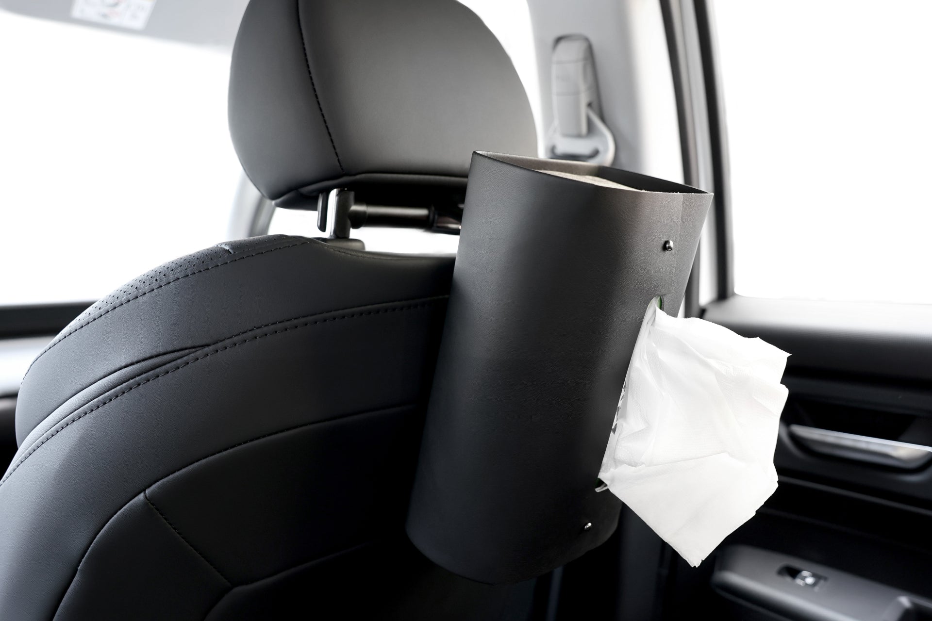 Close-up of a black car seat featuring the Universal MagSafe Car Seat Holder by JOWUA mounted on the headrest. White tissues are partially pulled out, ready for use. The car interior showcases a modern and sleek design with leather seating that perfectly complements the sophisticated setup.