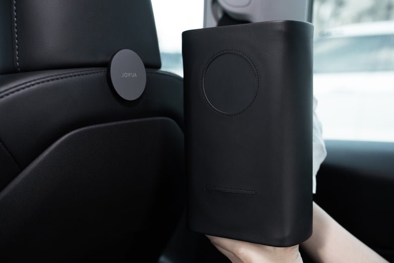 A person holds the sleek, black JOWUA Hook Bundle (Model S/X/3 2024+/Y Juniper 2025+) with a round "JOYFUL" label, easily installing this modern, minimalistic hook by the car seat in minutes for added front trunk storage.