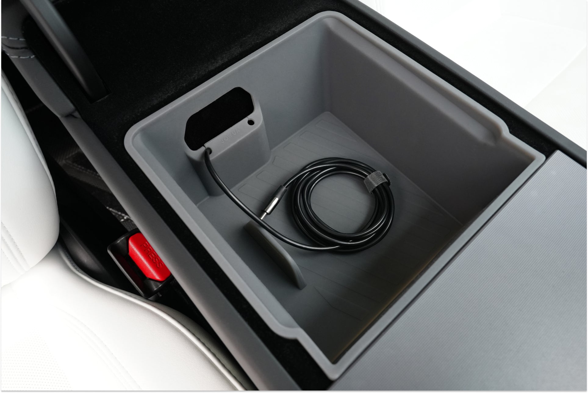 The JOWUA Armrest Organizer Set for Tesla Model Y Juniper 2025+ and Model 3 Highland 2024+ neatly stores a coiled black cable in the center console beside white leather seats and a red seatbelt latch.