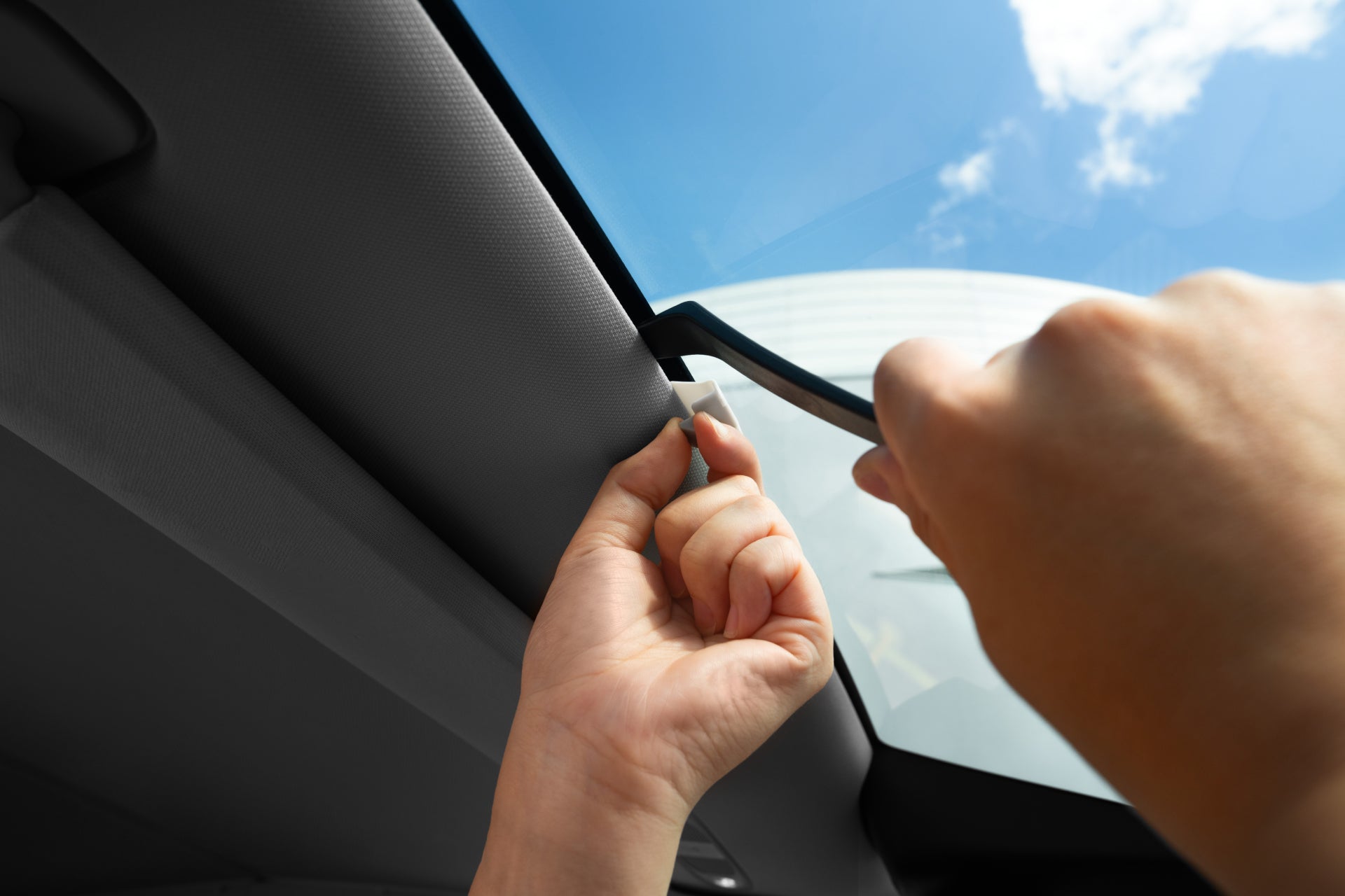 Close-up of two hands opening a Model Y sunroof, blue sky visible through the glass above, showcasing the UV protection from the JOWUA Windshield Sunshade for Model Y 2021-2024.