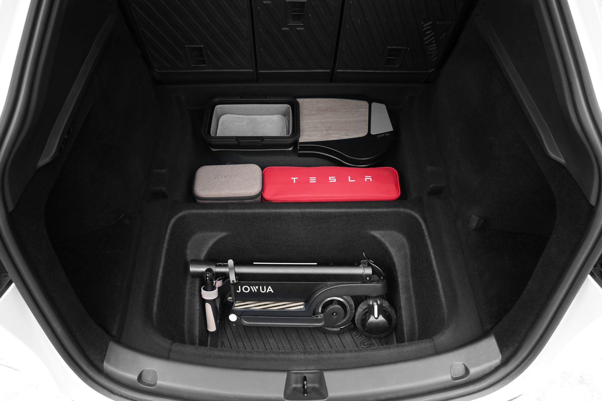 The open trunk of a Tesla Model Y features organized storage atop a JOWUA EasyShield Waterproof Trunk Liner + Rear Seats Back Cover Bundle (Juniper 2025+), showcasing durable TPE protection and neatly arranged items.