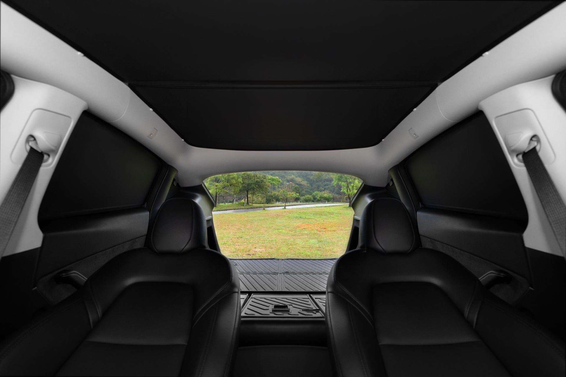 View from inside a car with black leather seats, looking out through the open trunk at grass and trees, where the JOWUA Side + Rear Liftgate Window Sunshade for Model Y 2021-2024 adds privacy and security.
