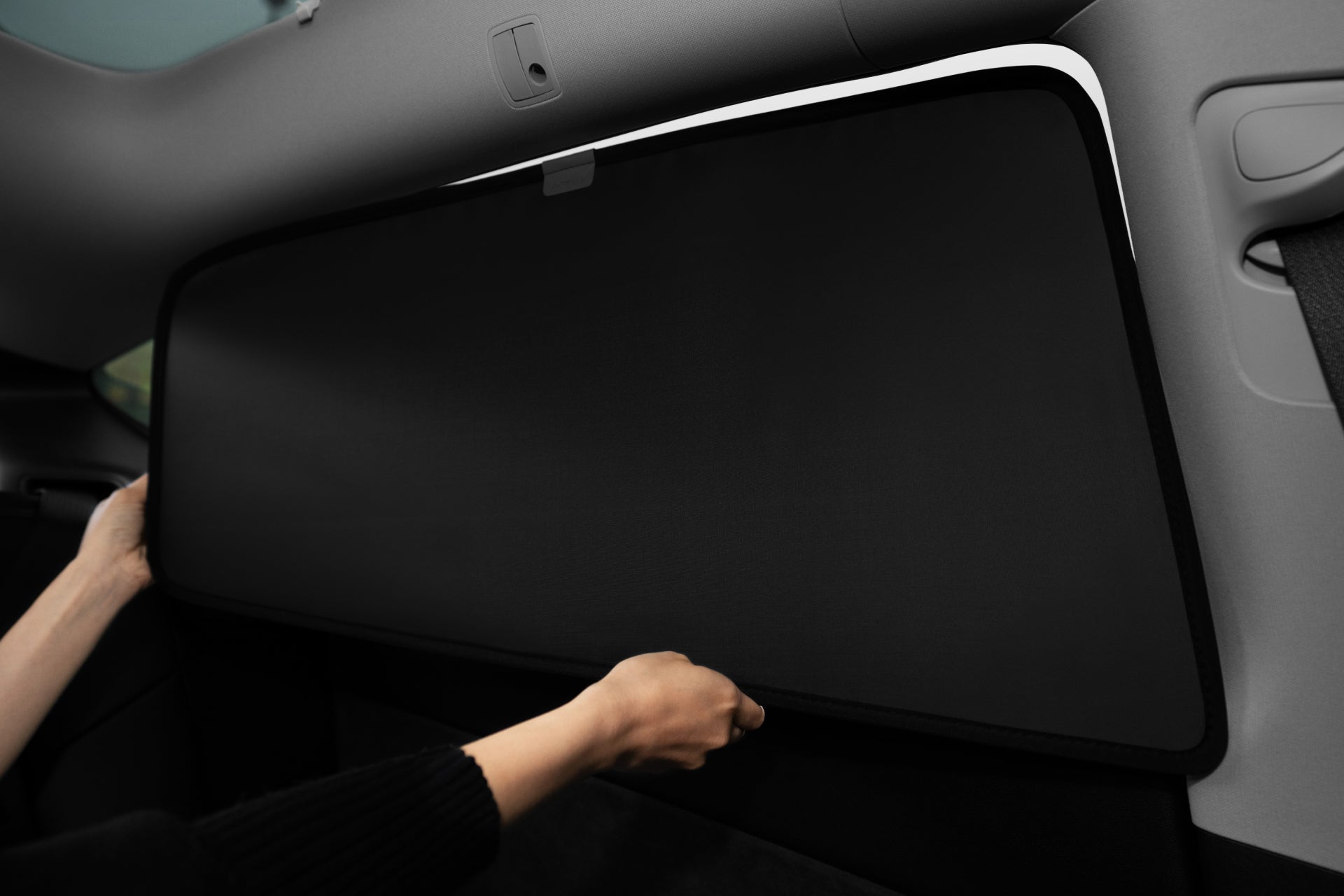 A person installs a JOWUA Side + Rear Liftgate Window Sunshade for Model Y 2021-2024, made of high-density fabric, on the rear window by holding the sunshade edges with both hands inside the vehicle.