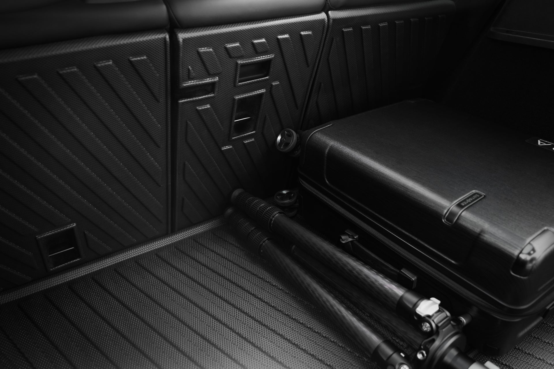 A black suitcase and folding tripod sit on a textured cargo floor in the rear of a Tesla Model Y, protected by the JOWUA Model Y (Juniper 2025+) EasyShield Waterproof Trunk Liner + Rear Seats Back Cover Bundle.