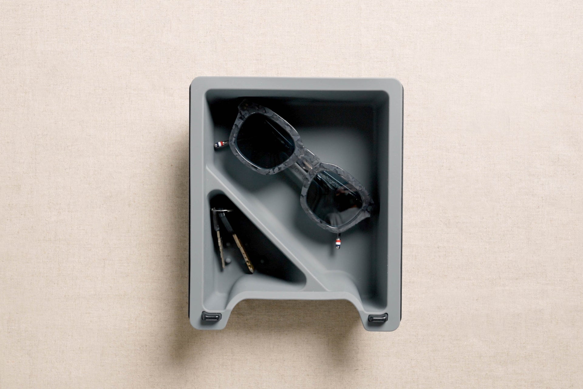 A square, gray LED Center Console Combo by JOWUA rests neatly on a light beige surface, perfectly sized to fit in the center console of your Tesla Model 3. It conveniently holds a pair of sunglasses and a set of keys with a keychain, keeping essentials within easy reach.