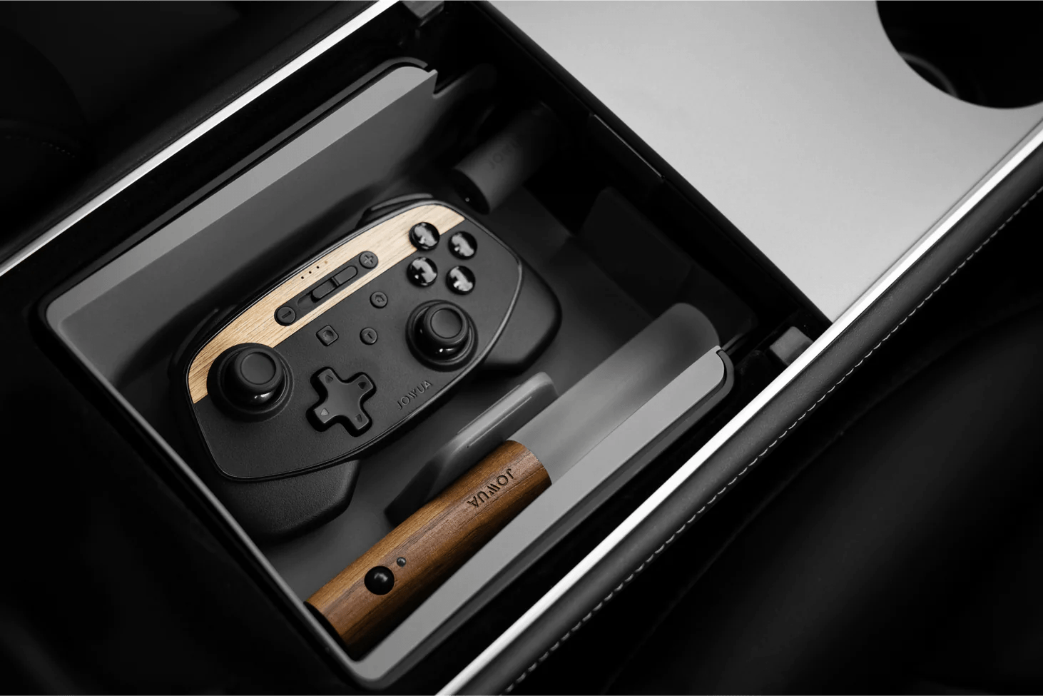 A gaming controller with wooden accents and a wooden-handled pen are neatly arranged in a metallic tray, reminiscent of the JOWUA LED Center Console Combo for Tesla Model 3/Y, inside a drawer or storage compartment.