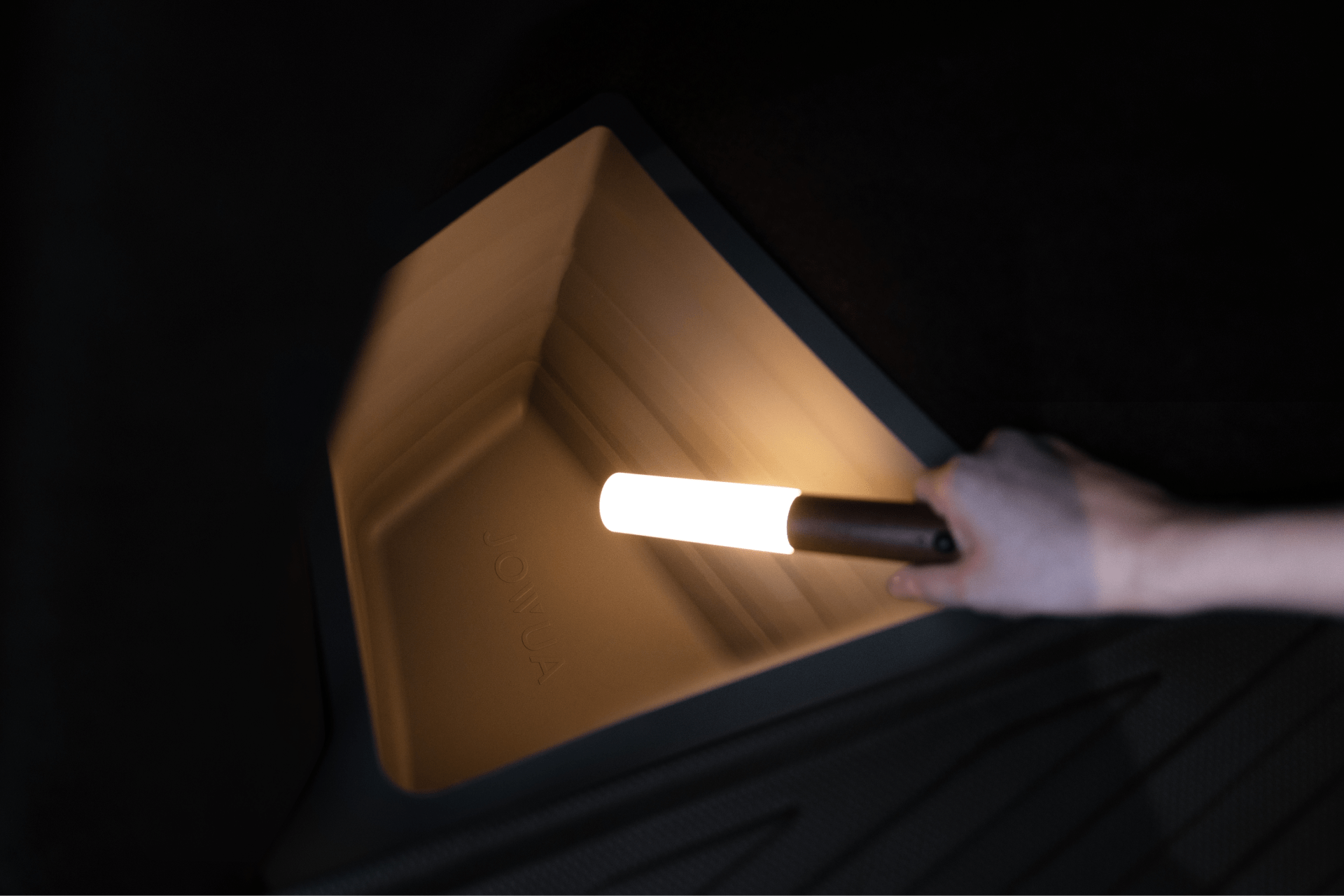 A hand with a cylindrical light reveals the spacious, angled storage of the 2025+ Model Y, perfect for installing the JOWUA Model Y Juniper Trunk Combo to protect your trunk.