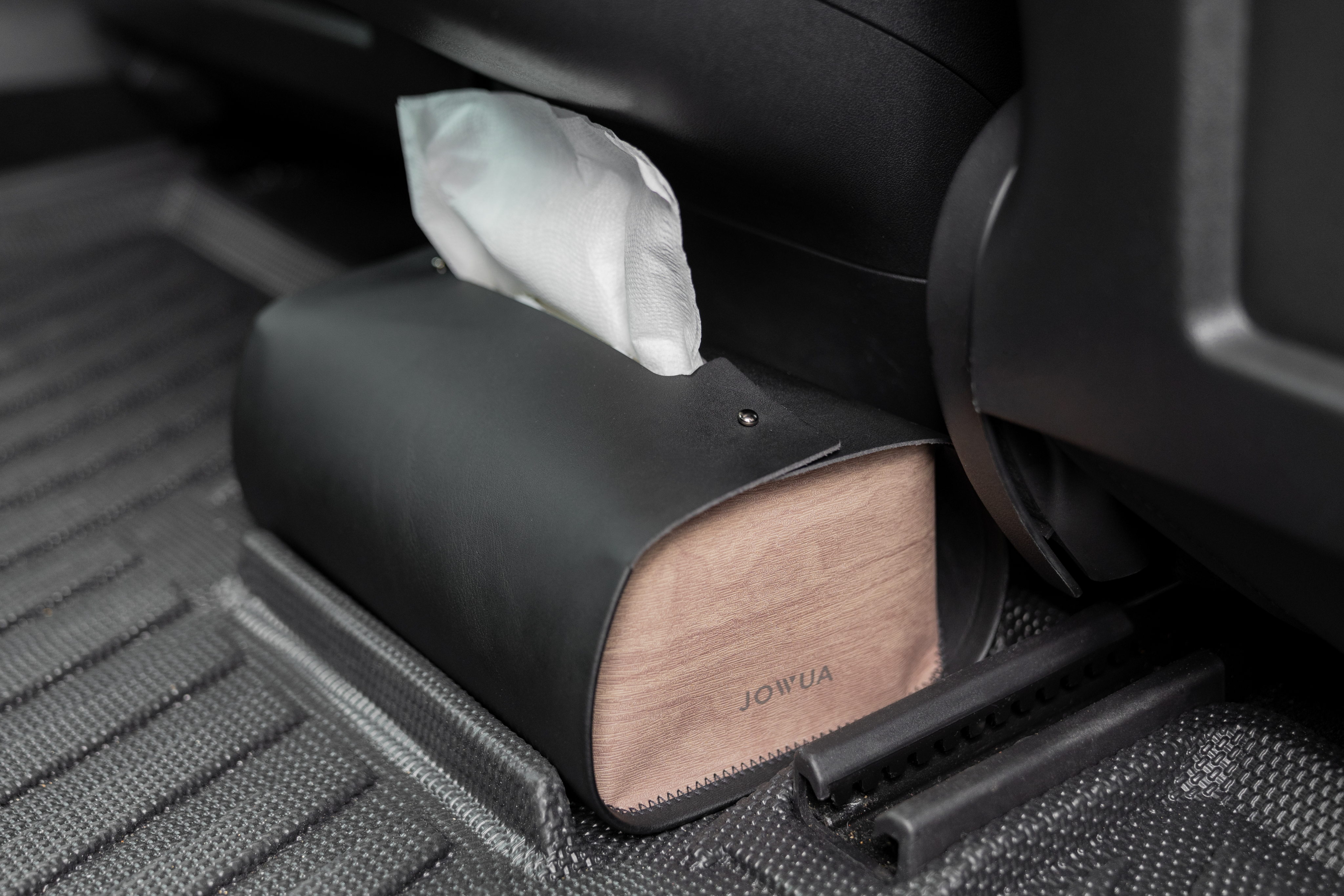 A product called the MagSafe Tissue Box Cover by JOWUA elegantly sits on a textured car floor mat. Made from premium microfiber leather, it's the perfect accessory for your Model 3/Y, with tissues neatly protruding from the top.