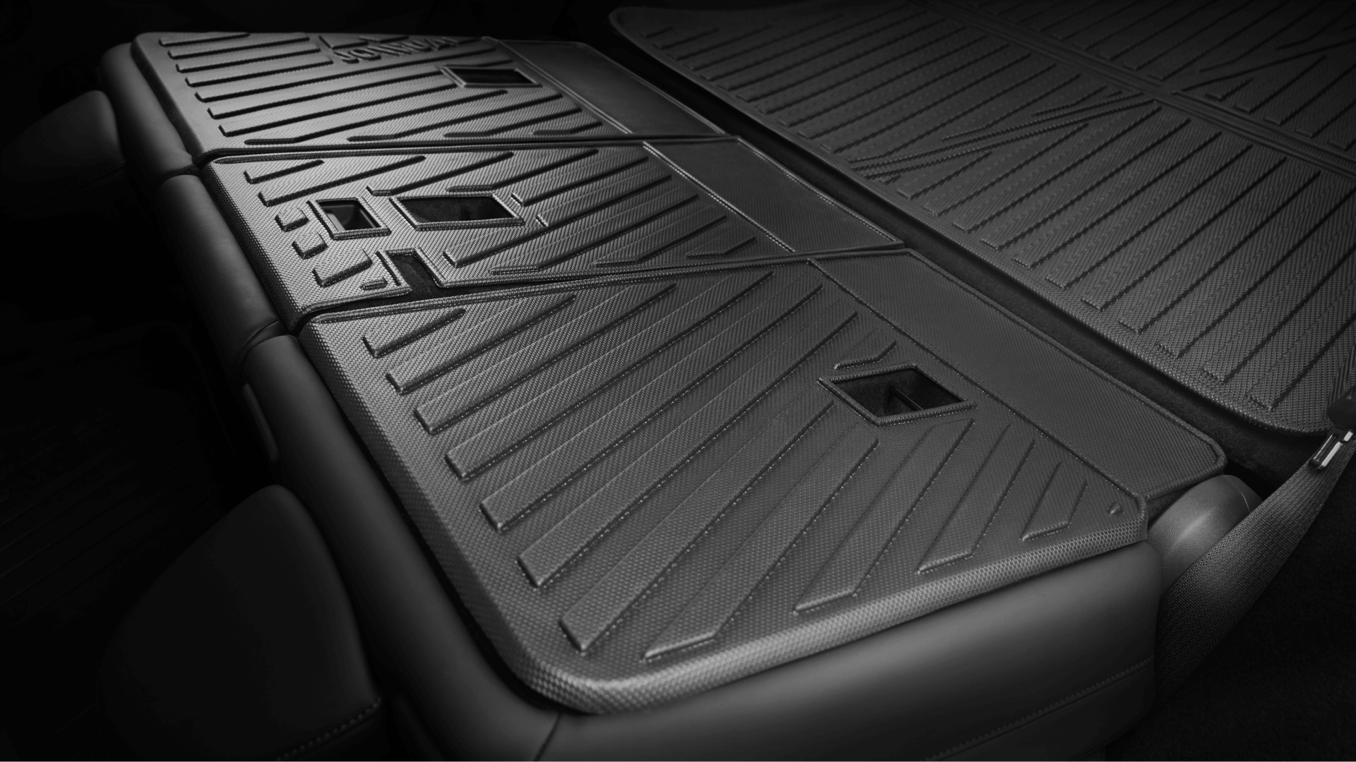 Close-up of JOWUA Model Y Trunk Combo (2018-2024) installed: black rear seat backs folded flat, revealing textured, geometric surfaces with rectangular cutouts—ideal for trunk liners and other storage accessories.