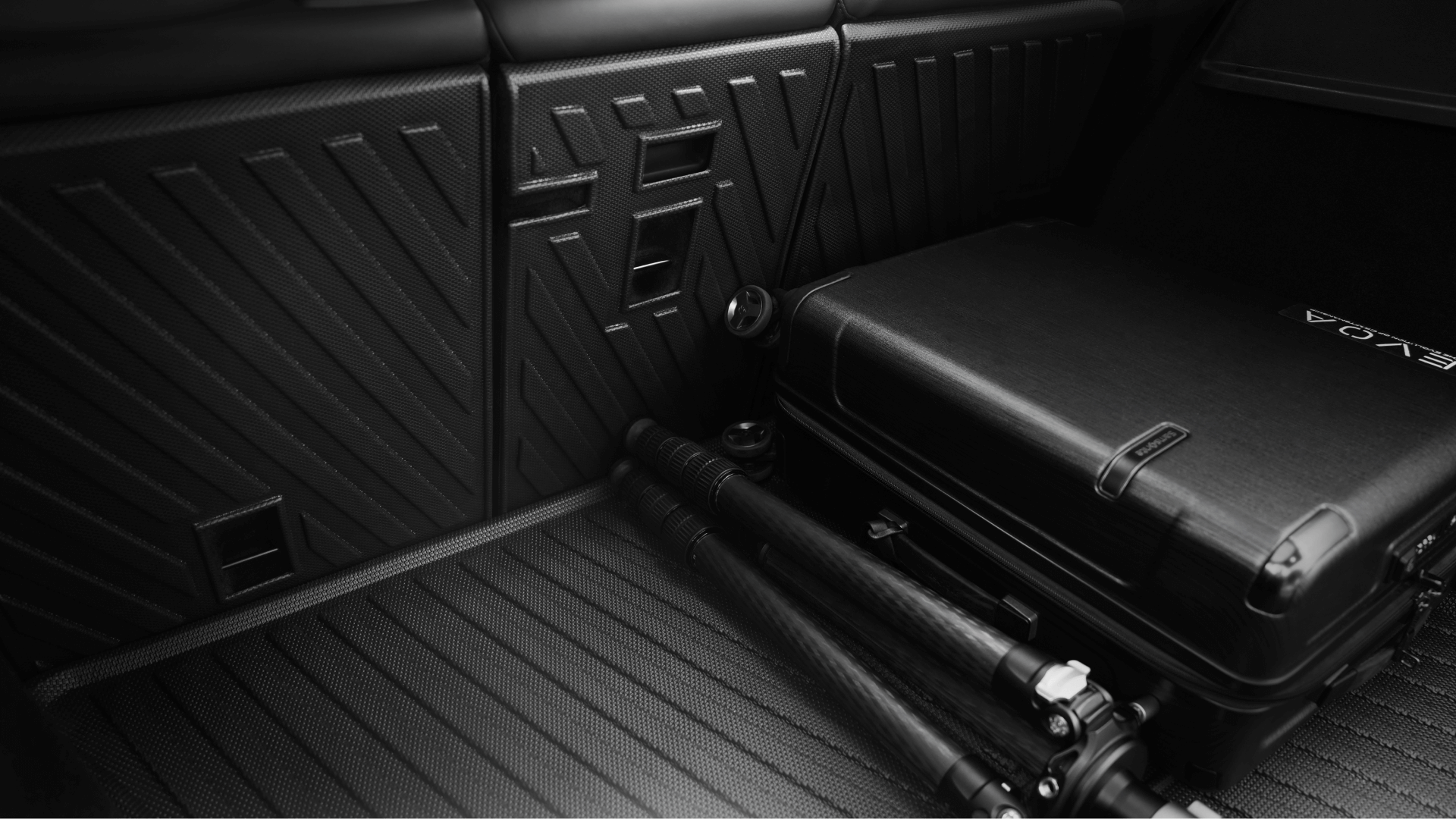 A JOWUA Model Y Trunk Combo (2018-2024)—including a black hard-shell suitcase and folded tripod—is displayed on the textured cargo floor with patterned trunk liners, offering ideal storage for Tesla Model Y owners.