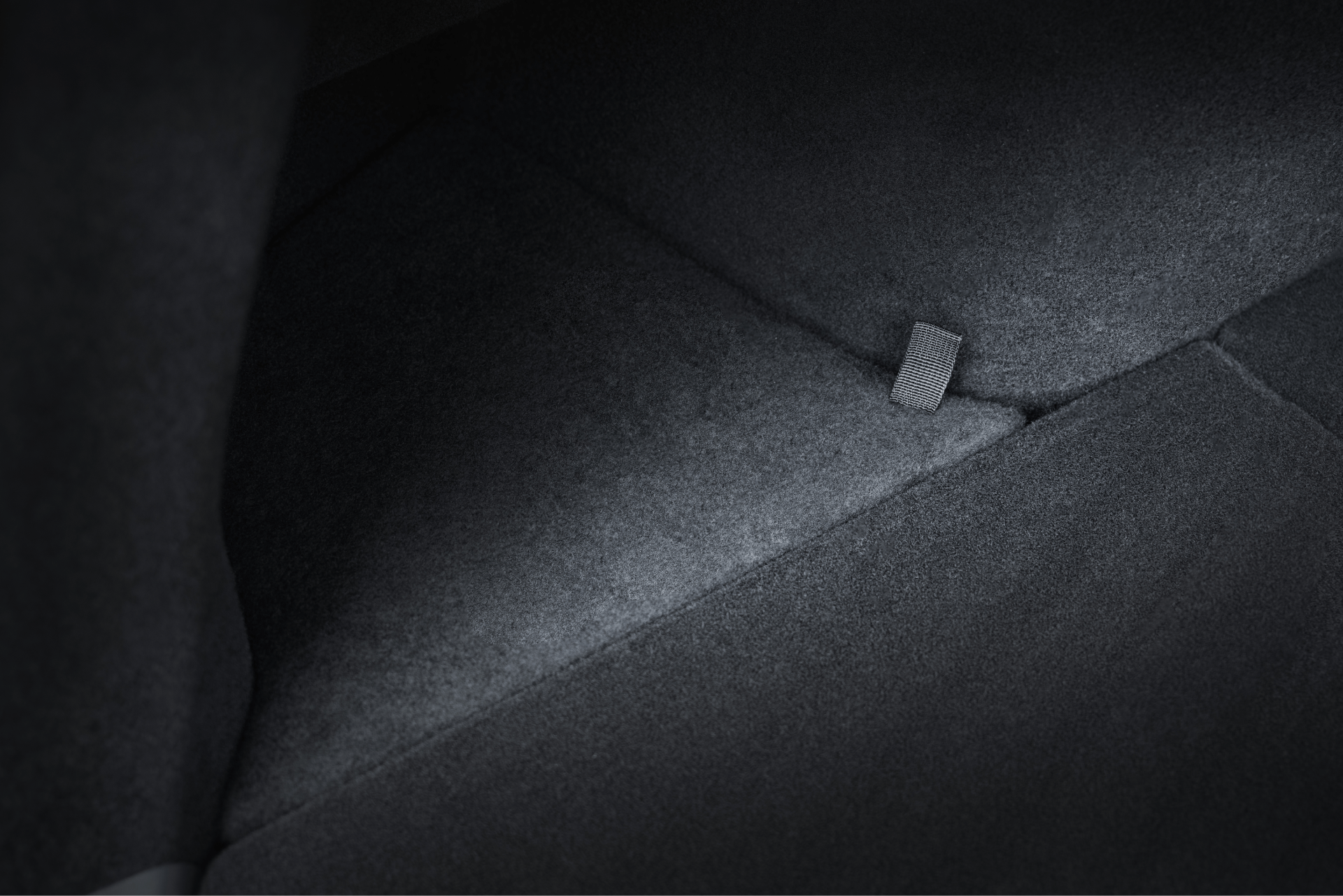 Close-up of a car's dark gray carpeted interior reveals a small fabric pull tab—a detail featured in the JOWUA All-in-One Interior Upgrade Set for Model Y Juniper (2026+).