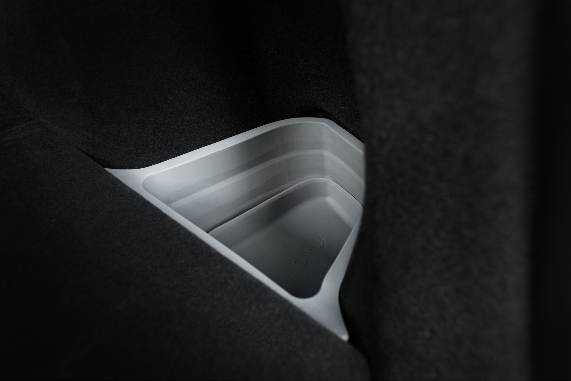 A close-up of the JOWUA Trunk Storage Bins Bundle for Model Y (2018-2024) shows its gray, rectangular silicone design with smooth edges and layered sides, neatly fitting between plush car interiors and emphasizing a clean, minimal look.