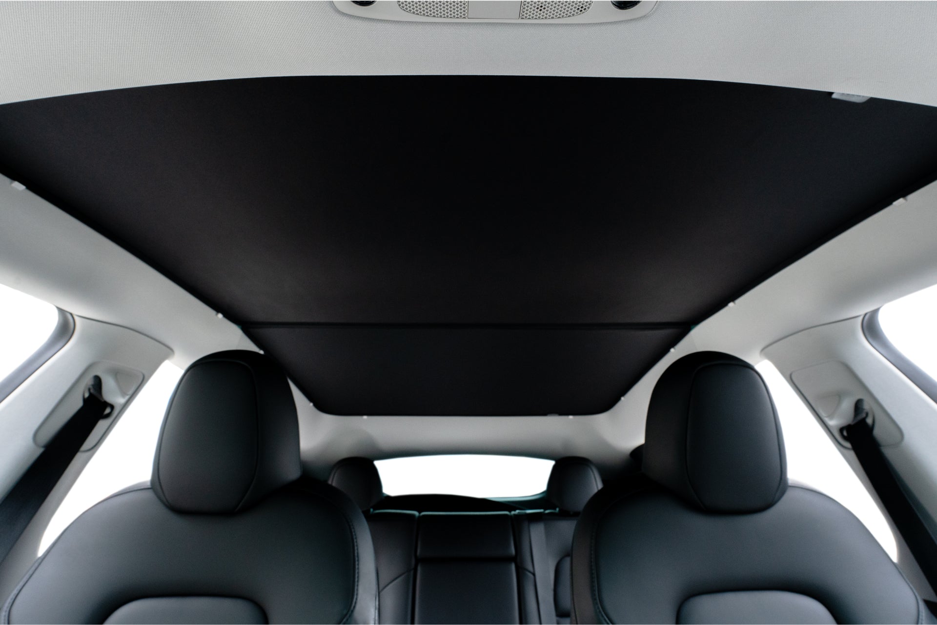 The interior view of the car highlights sleek black leather seats and a panoramic sunroof, partially covered with JOWUA's Model Y Ultimate Sunshade Bundle. The roof liner is light-colored, complemented by modern headrests showcasing Dark Matter mesh fabric for both style and UV protection.
