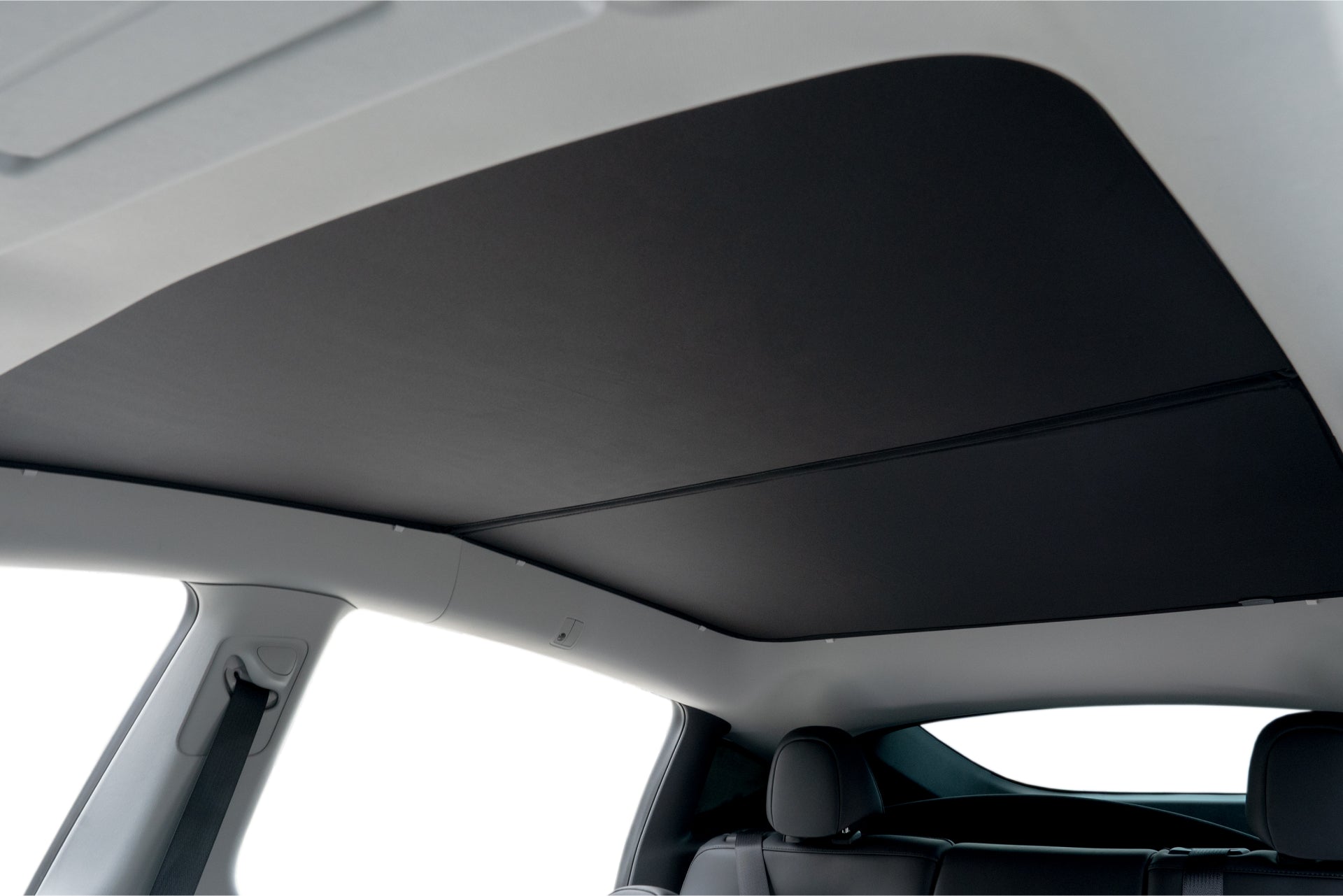 Experience the car interior with the Model Y Ultimate Sunshade Bundle by JOWUA, showcasing a closed panoramic sunroof equipped with a black Dark Matter mesh fabric shade that provides UV protection. The view highlights the back seats and a portion of the rear window, emphasizing the vehicle's remarkable light and dark color contrast.