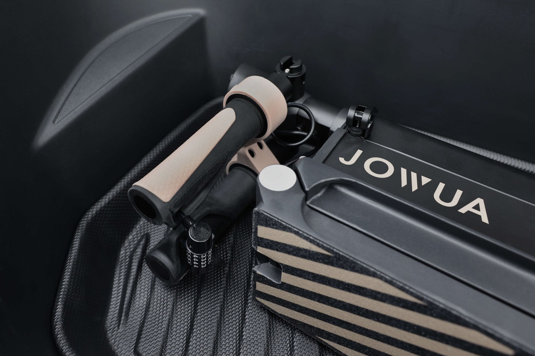 A close-up of a foosball grip, showcasing black and beige colors, alongside a JOWUA-branded box inside a vehicle's trunk. The box features a striped design with the JOWUA logo prominently displayed, ingeniously concealing an anti-theft padlock. The interior reveals a textured, lined pattern on the Folding Electric Scooter (Long Range) for Tesla (S3XY).
