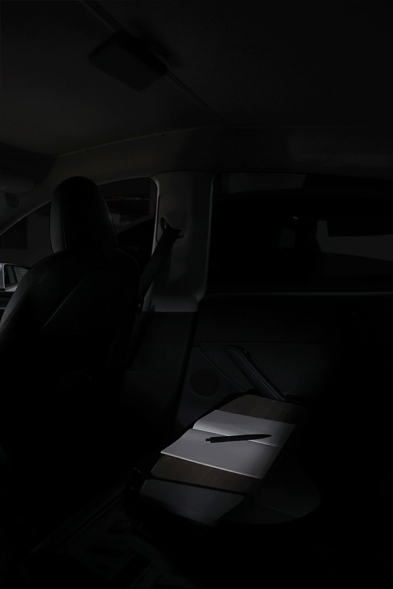In the softly lit car interior, a white package on the passenger seat is highlighted by a narrow beam of light, casting subtle reflections on the JOWUA LED Center Console Combo - Tesla Reengineered Model 3 Highland (2024+) made of premium silicone nestled in the center console system.