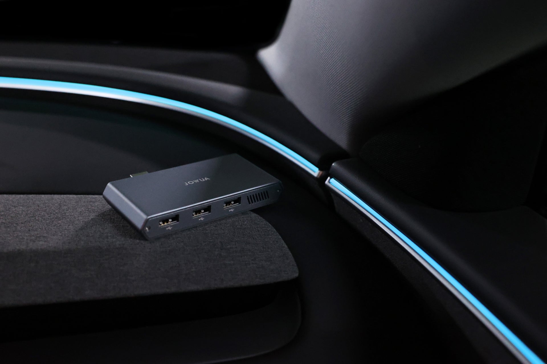 A JOWUA Tesla 1TB SSD + 3-Port HUB rests on a dark car surface, glowing under blue ambient light—ideal for Sentry Mode storage or expanding your Tesla’s connectivity.