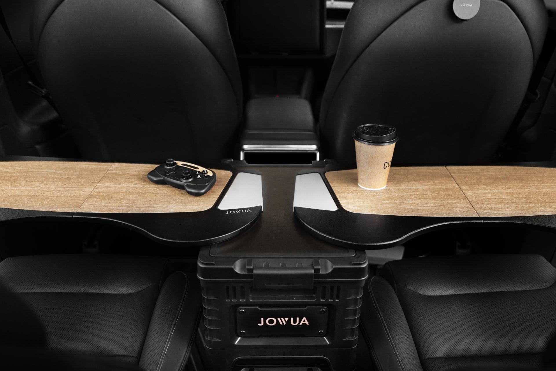 Two wooden folding trays sit between car seats—one holds a video game controller, the other a coffee cup. Below is a black JOWUA 30L Stackable Storage Box and Trunk Organizer for Teslas, blending style and organization into your ride.