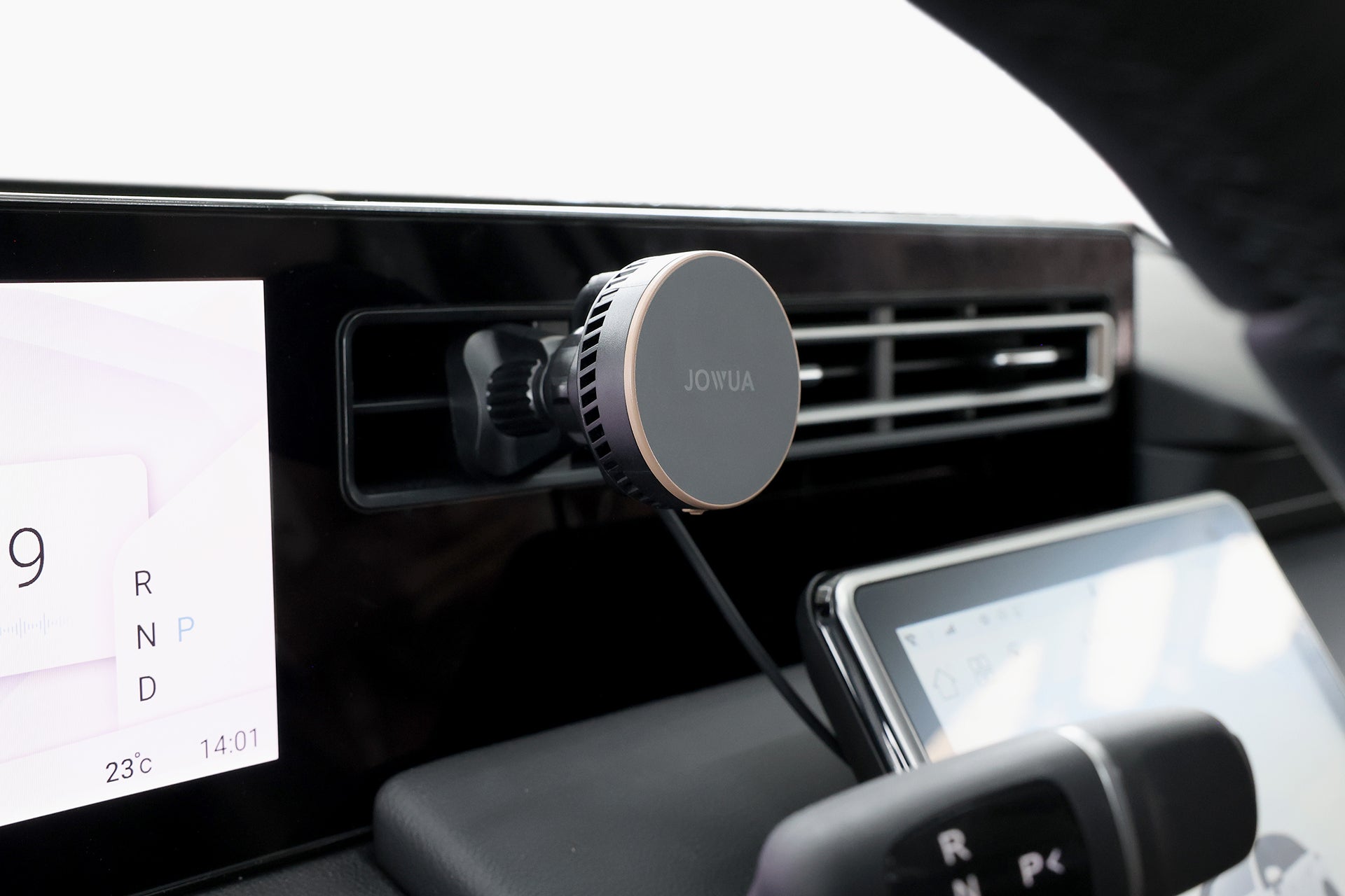 A close-up of a car dashboard shows the JOWUA Active Cooling Universal MagSafe Car Mount for Air Vents, with MagSafe wireless charging, attached to an air vent. A digital display and part of the steering wheel are also visible.