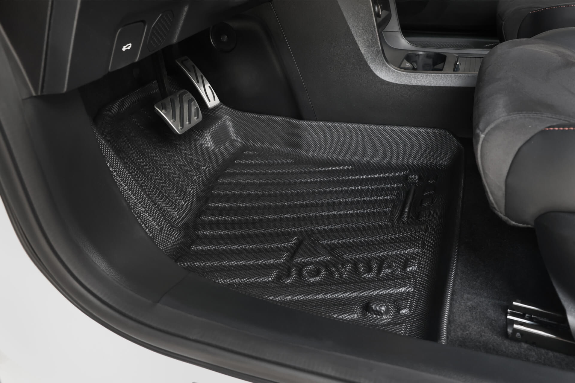 Close-up of a MG MG4 driver-side footwell featuring a black textured JOWUA All Weather Floor Liner and metal accelerator and brake pedals. The custom-fit liner complements the vehicle’s clean, modern interior.