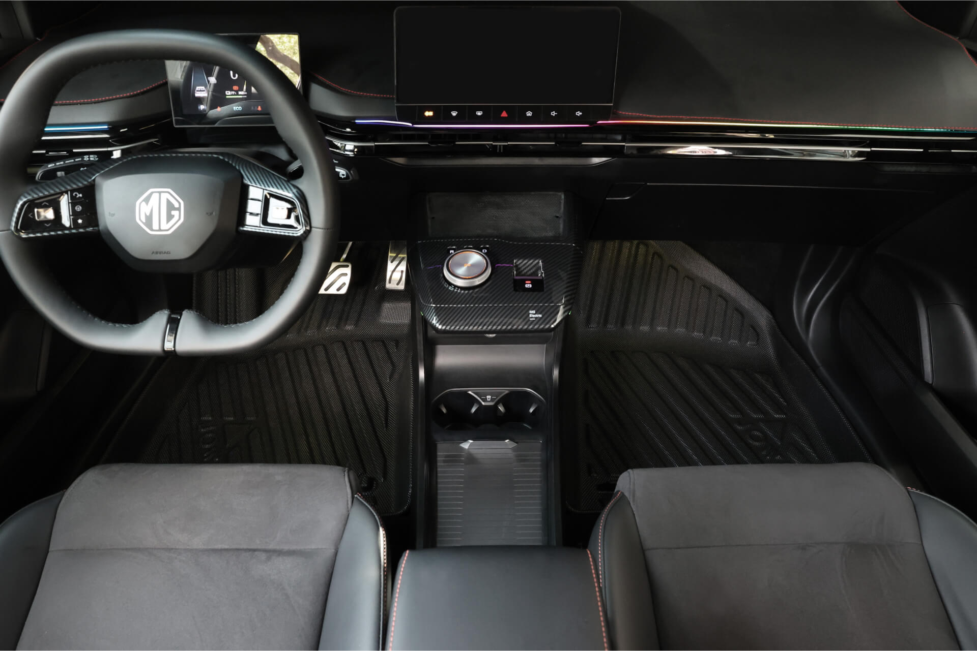 Interior view of an MG4 with a steering wheel, wide digital dashboard, control knob, cup holders, and black leather seats with red stitching. A JOWUA All Weather Floor Liner custom fit for MG4 enhances its modern and minimalist design.