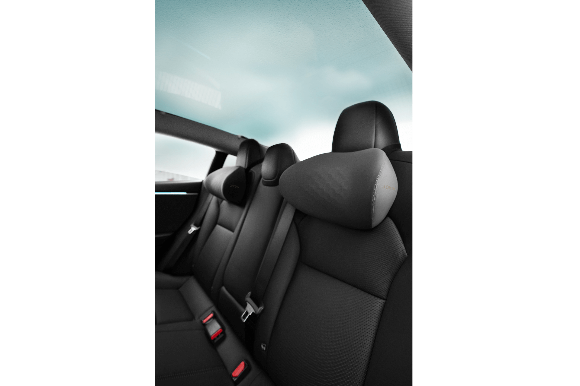 The image features the JOWUA Car Neck Pillow on black leather backseats with ergonomic headrests and seat belts, viewed from the side. The car’s rear window and roof are visible, revealing a bright sky outside.