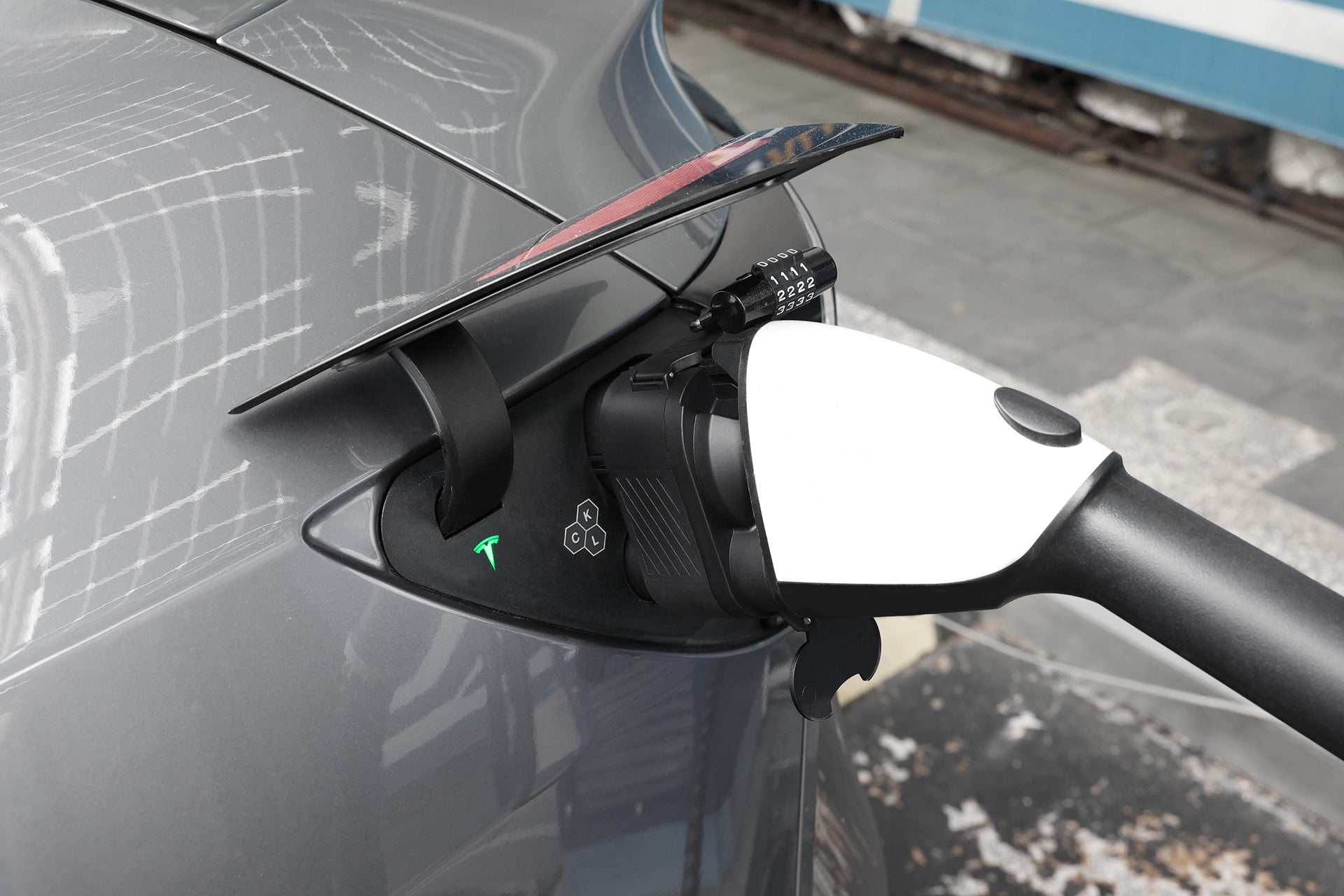Close-up of a grey electric car charging outdoors with the JOWUA CCS1 to CCS2 DC & AC Combined Adapter plugged in, a green indicator light glowing to show active fast charging.