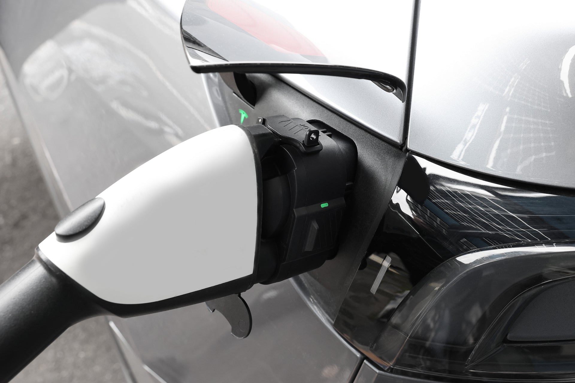 Close-up of a JOWUA CCS1 to CCS2 DC & AC Combined Adapter connected to the rear port of a silver electric vehicle during DC fast charging, with charger indicator lights visible.
