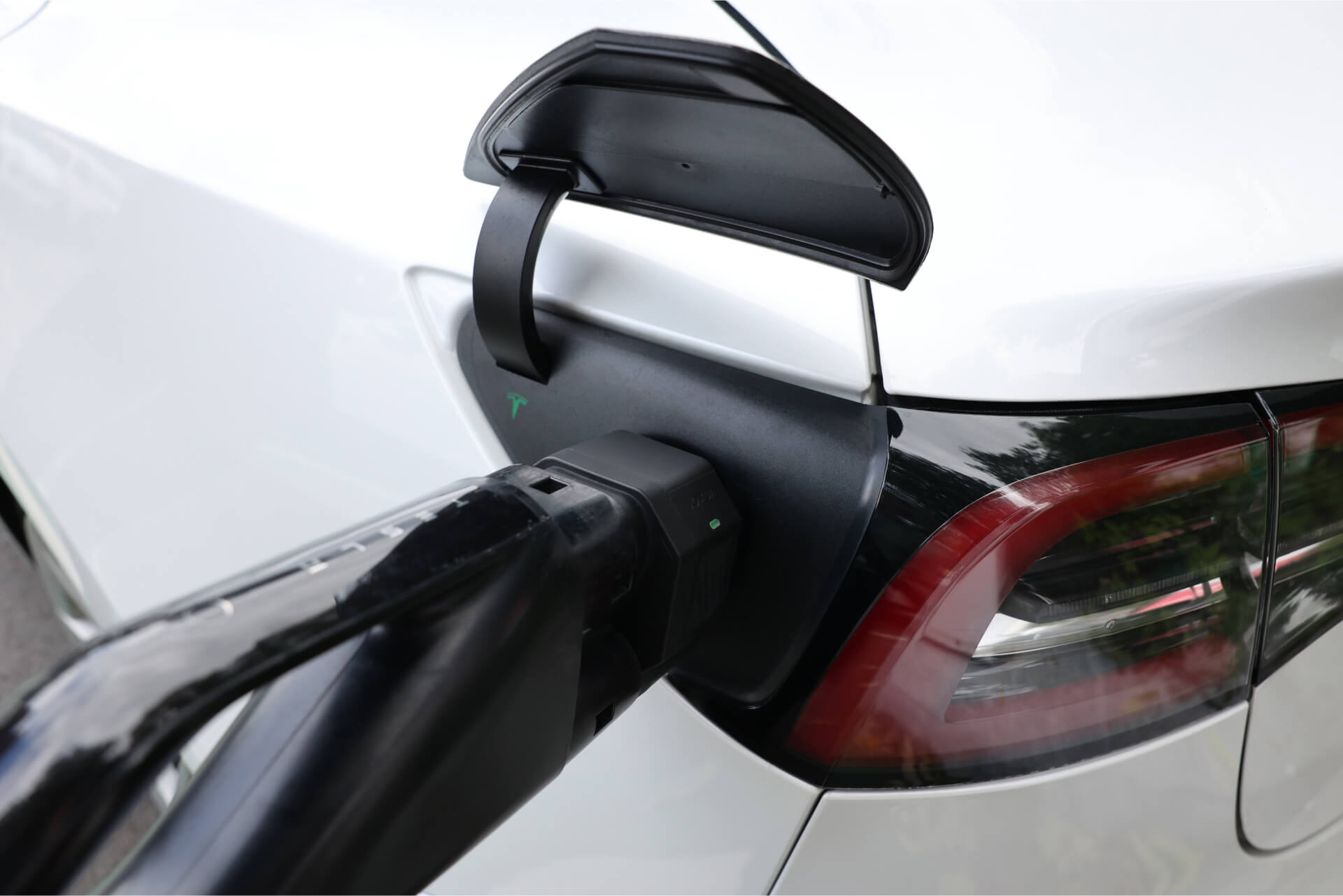 Close-up of a charging cable plugged into a white EV using the JOWUA CCS2 to NACS DC Charging Adapter, with the open port cover and rear tail light visible, highlighting seamless Tesla CCS charging compatibility.