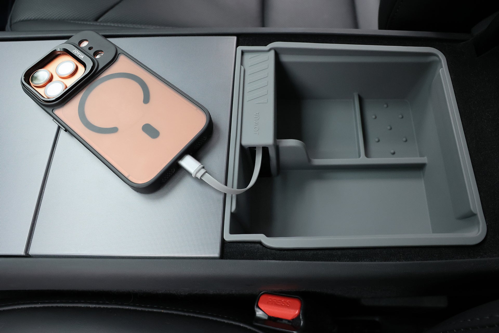 A smartphone charges in a Tesla Model 3’s center console beside the JOWUA Center Console Organizer Set with Power HUB (2024-2026+), with the red seatbelt release button visible in front.