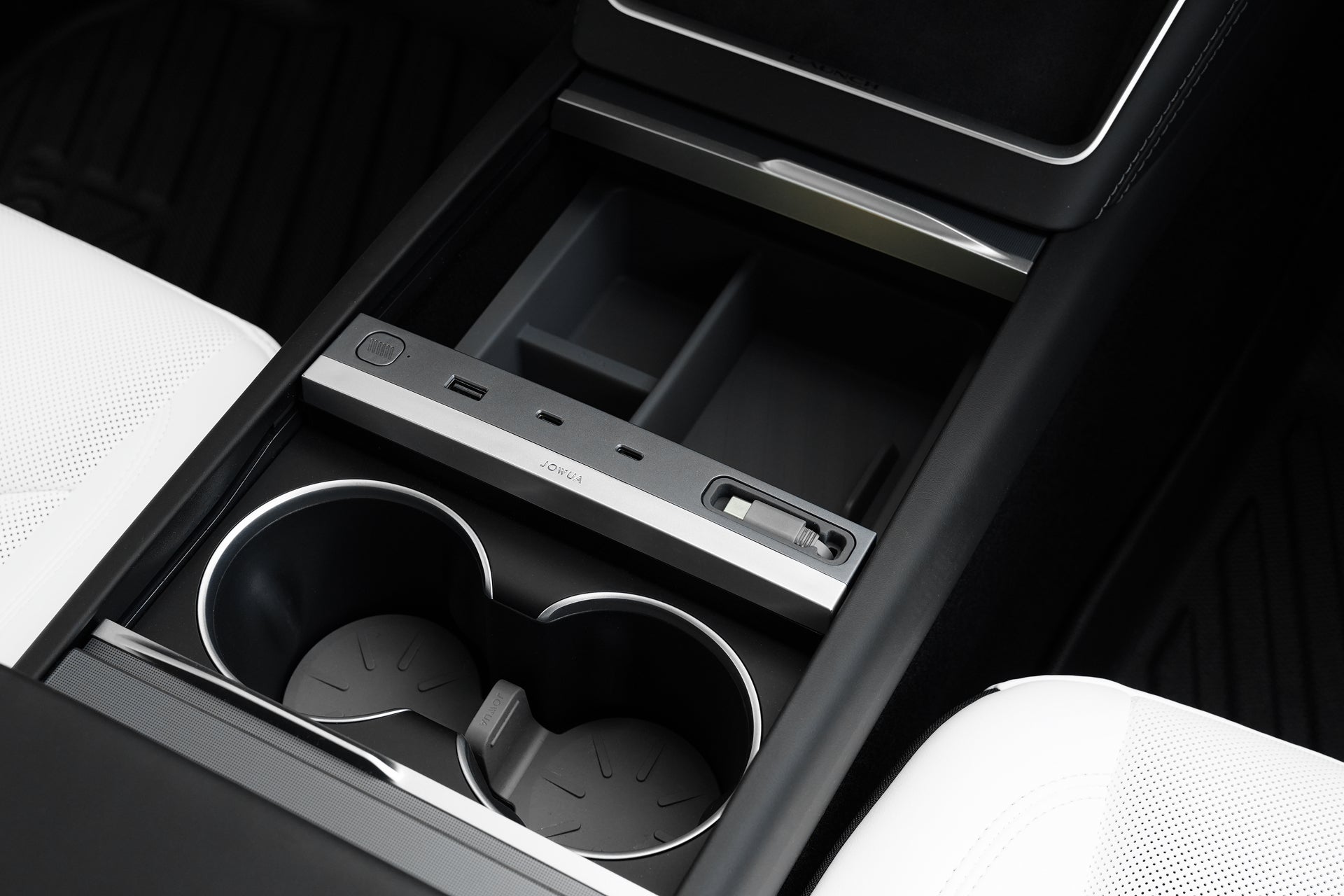 Close-up of a Tesla Model Y 2026 center console with two cup holders, an open storage compartment, and the JOWUA All-in-One Interior Upgrade Set – Model Y Juniper (2026+), featuring USB ports and a slot between white seats.