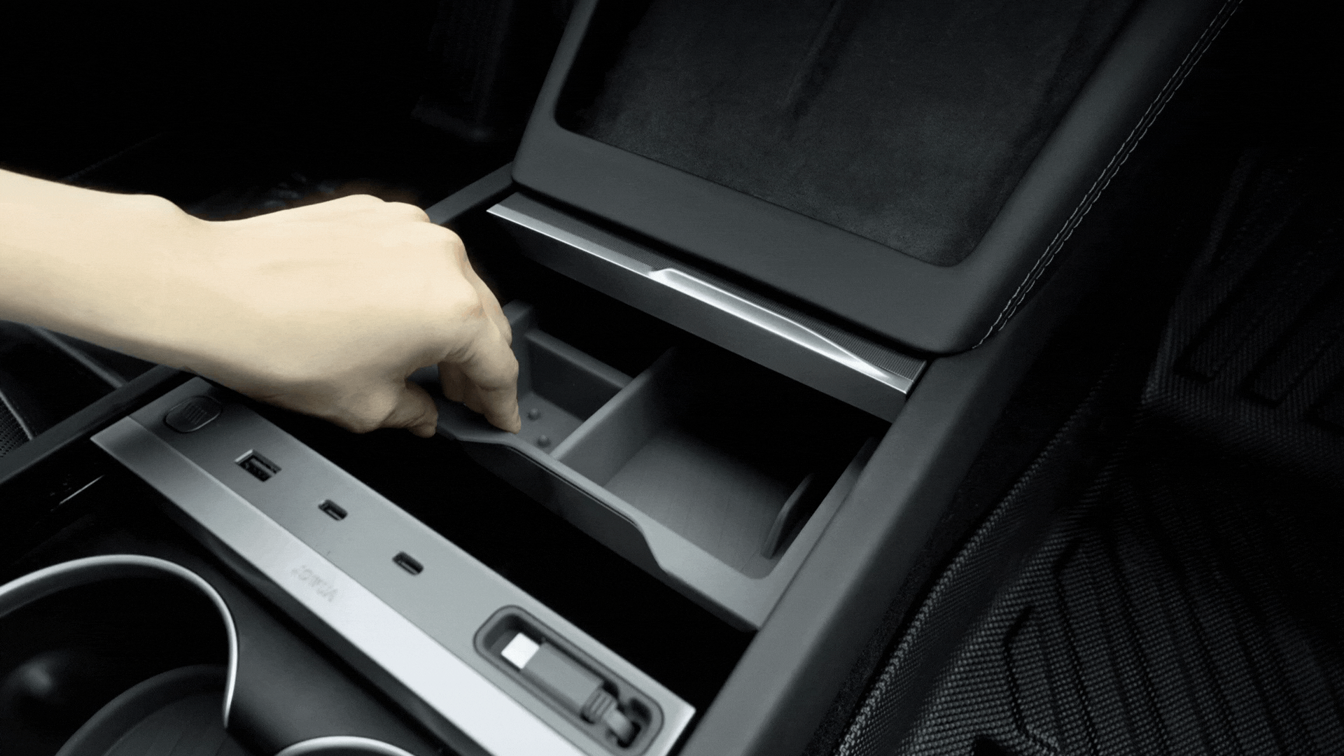 A hand pulls out a small tray from the JOWUA Premium Interior Essentials Set (RHD) for Model Y Juniper (2025+), revealing extra storage compartments beneath, with cup holders and USB ports nearby.
