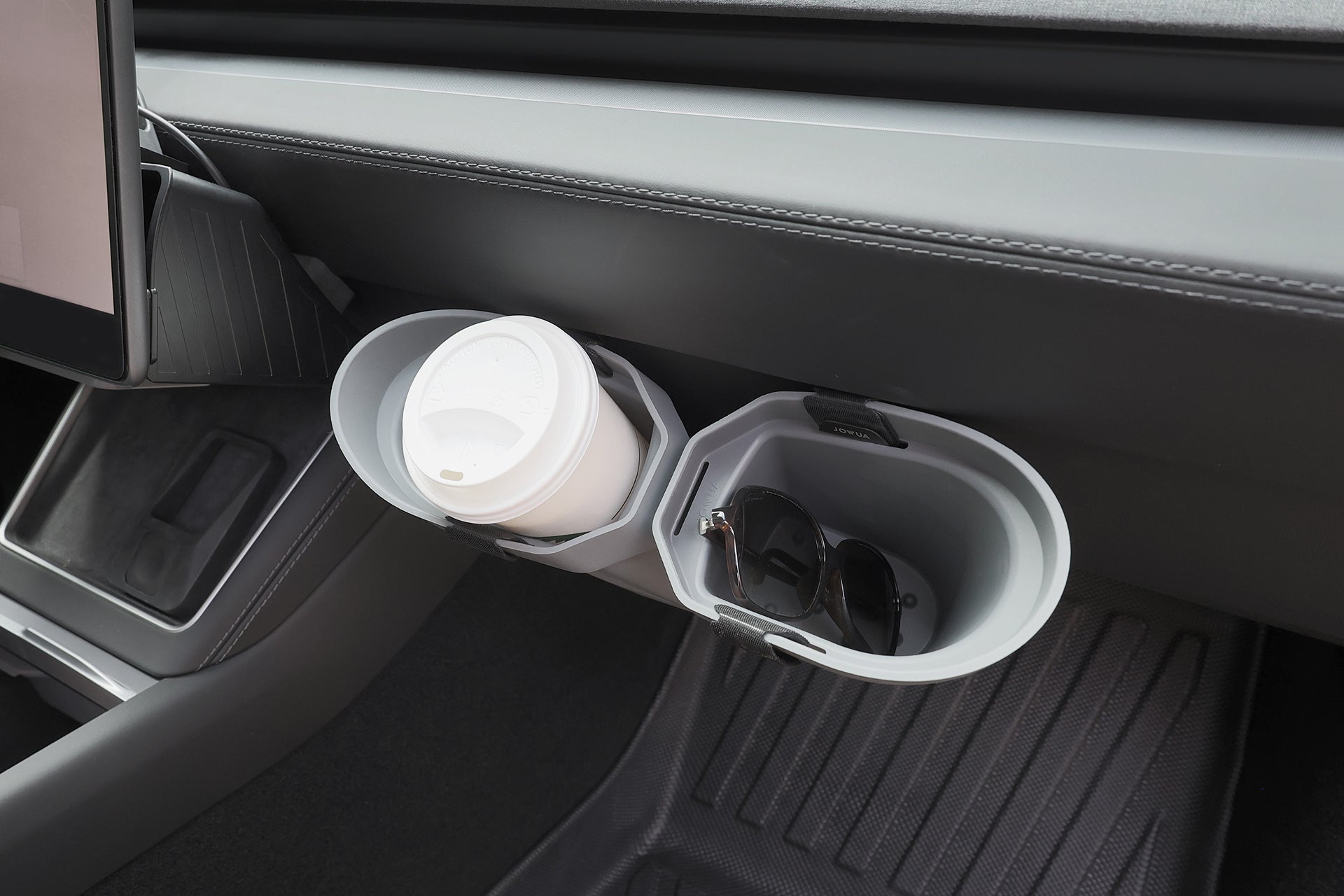 A close-up of a car’s interior shows two cup holders—one with a white coffee cup and the other with black sunglasses. Near the dashboard, a JOWUA Door Side Storage Box (Set of 2) is also visible, along with a floor mat.