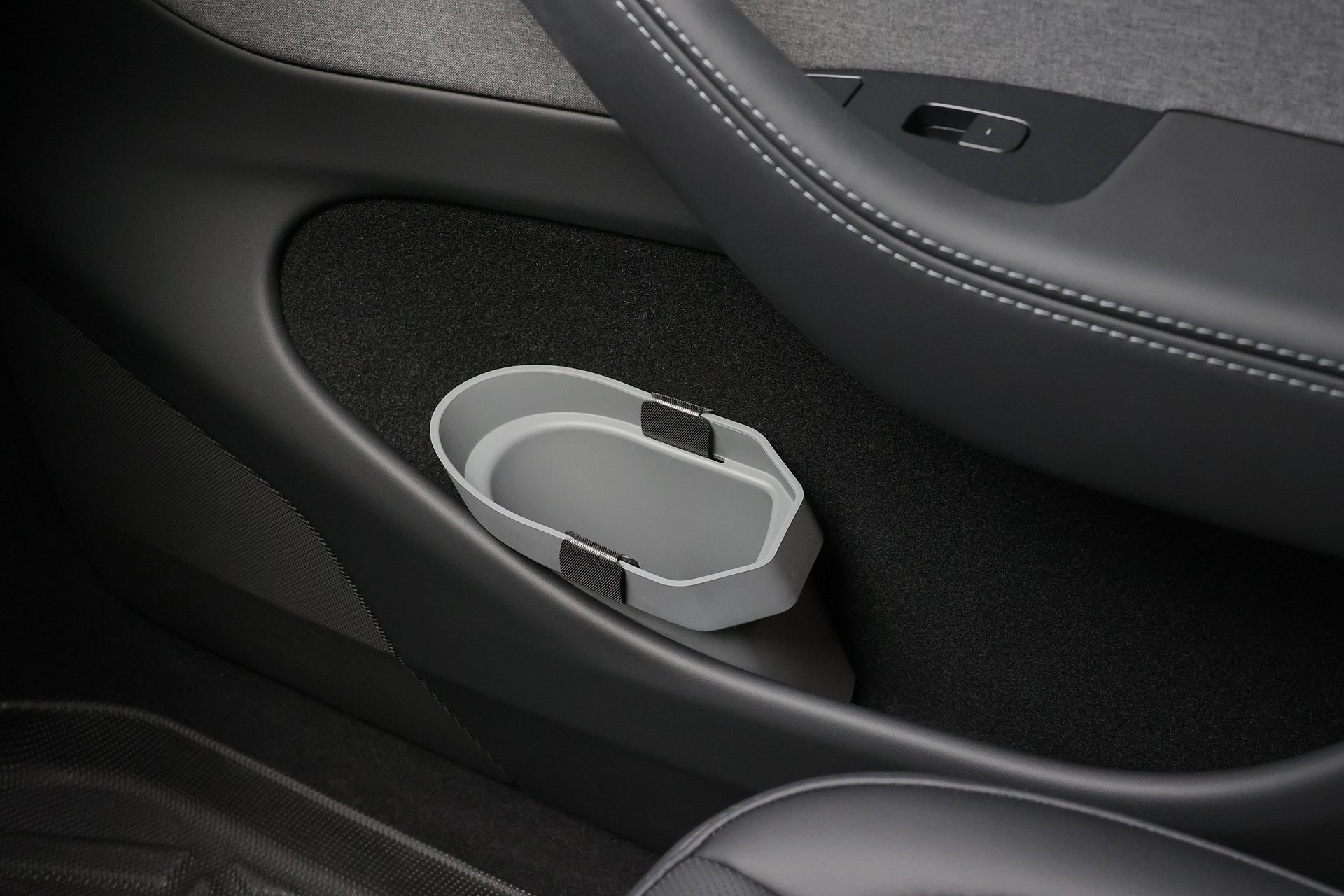 Close-up of a JOWUA Door Side Storage Box (Set of 2) in gray silicone, attached to the lower car door panel above the black carpet and next to the seat.