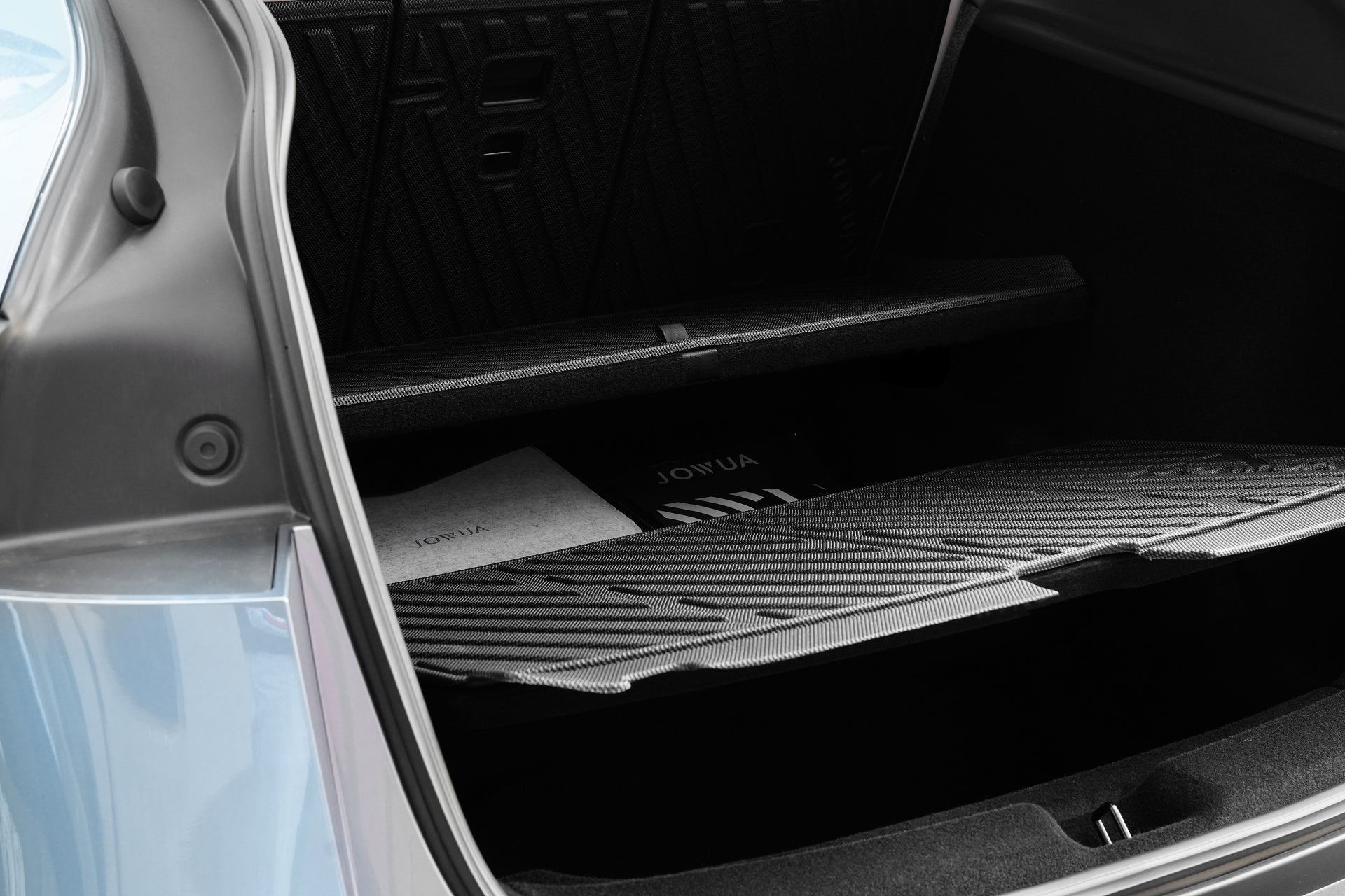 A close-up of the open trunk of a Tesla Model Y (Juniper 2025+) shows organized compartments protected by JOWUA EasyShield Waterproof Trunk Liner + Rear Seats Back Cover Bundle, with a visible "JOWUA" folder inside.