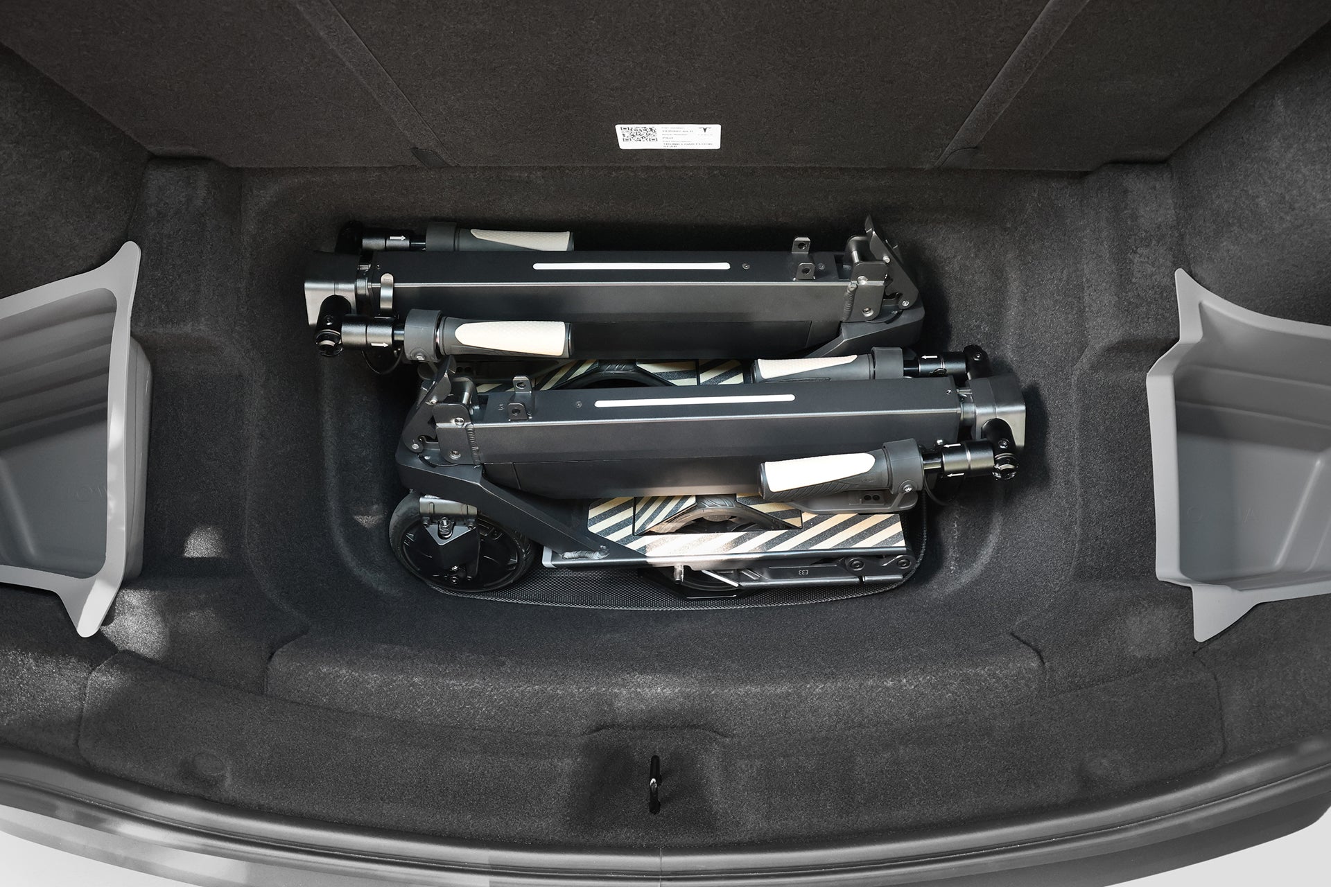 A close-up of a car’s frunk shows two JOWUA Folding Electric Scooter|Performance models with long-range batteries, neatly stored side by side.
