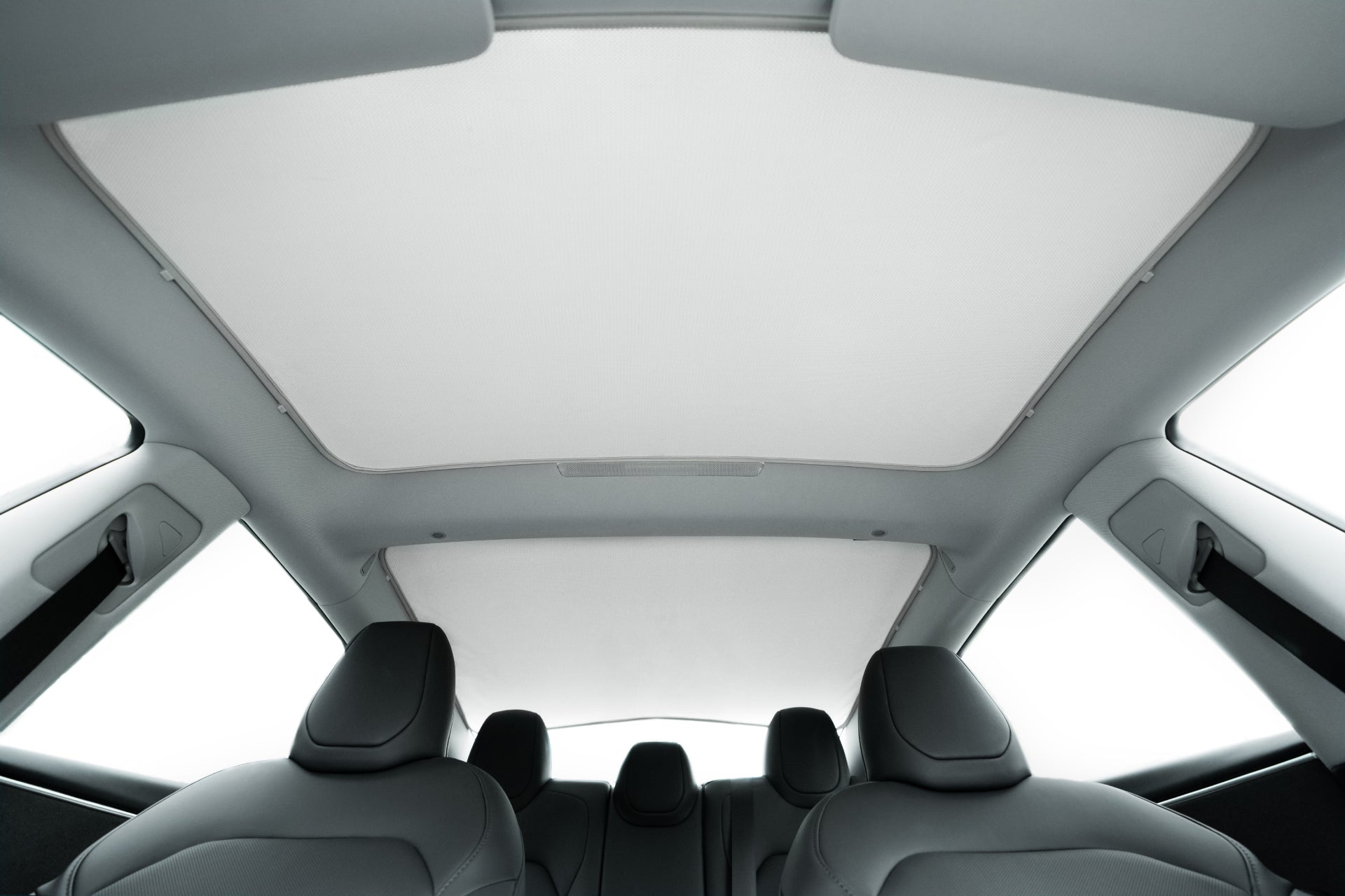 View from the back seat of a modern car with five headrests and a large panoramic roof fitted with the JOWUA Model 3 (2024+ Highland) Glass Roof Sunshade (US Version) for UV protection, all set in a sleek, minimalist light gray interior.
