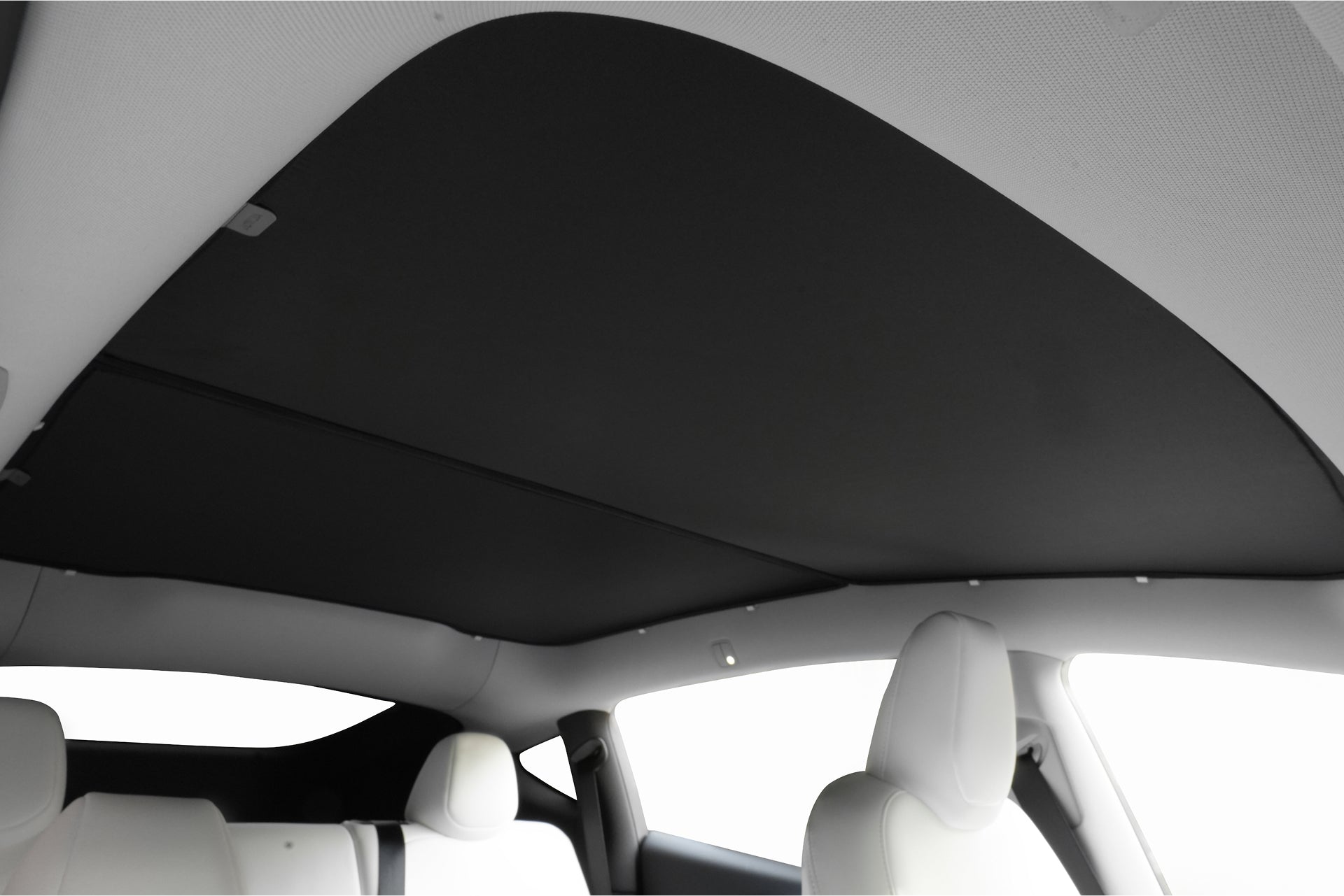 Interior view of a car featuring the JOWUA Ultimate Sunshade Bundle Model Y Juniper (2025+) installed over the glass roof, with white seats. This blackout sunshade offers UV protection while enhancing the minimalistic design.