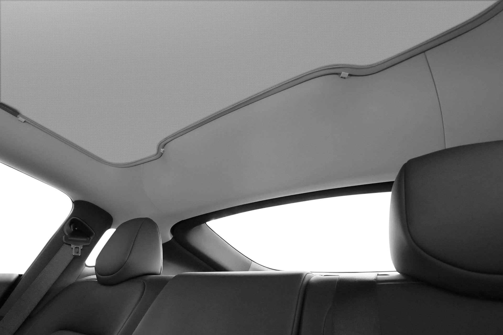 Interior view of a car's back seat with black leather seats and headliner, featuring the JOWUA All Model Y Glass Roof Sunshade (Juniper 2025+ / 2021-2024) clipped to the seatbelt for added UV protection.