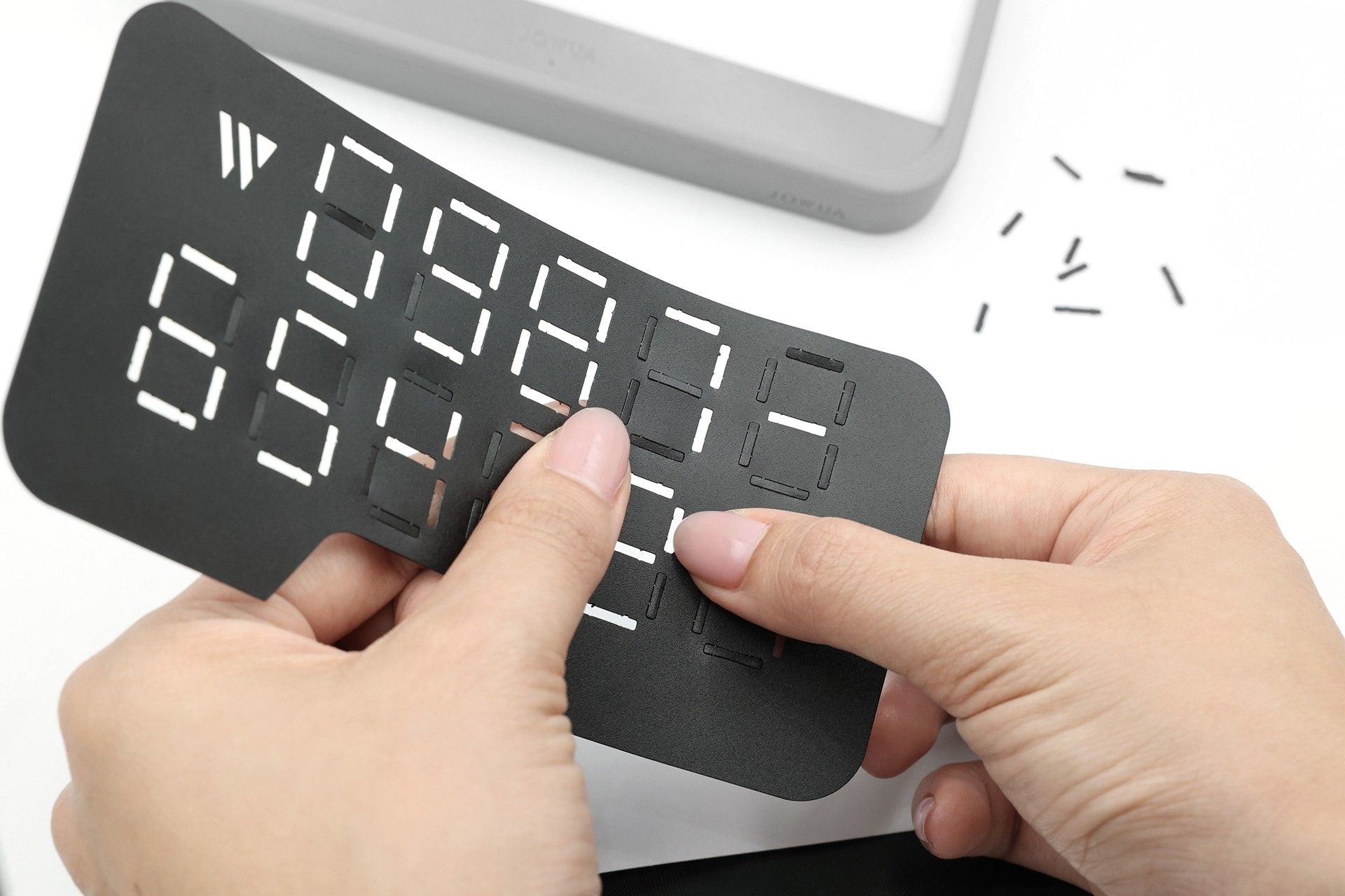 A person removes white plastic segments from the thin, black face of a JOWUA MagSafe LED Light with Light Stencil Set—featuring a sleek gray body reminiscent of Tesla wireless charging pads—with additional light stencils visible in the background.