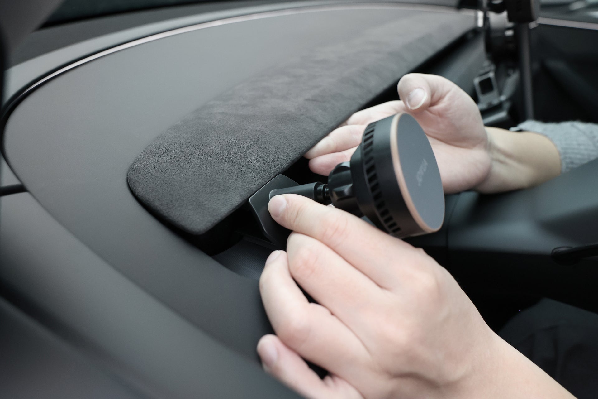 A person installs the JOWUA Active Cooling MagSafe Car Mount for Air Vents (Model 3 Highland & Model Y Juniper) onto a car dashboard, with a close-up on the mount and dashboard surface.